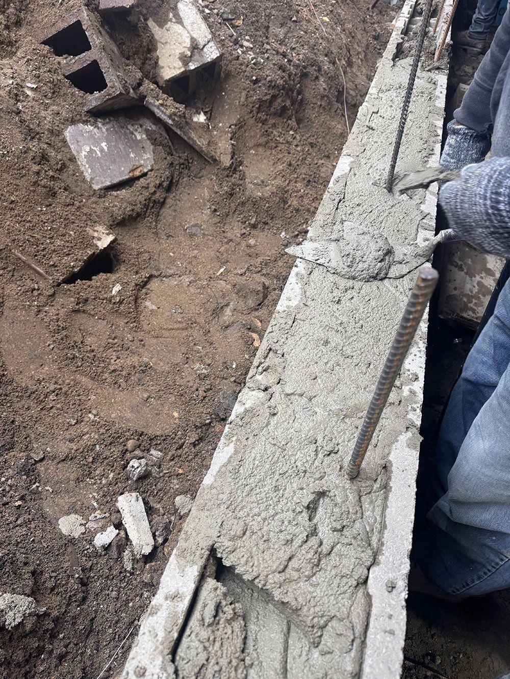 A person smoothing wet concrete in a wooden form with rebar reinforcements; outdoor construction scene.