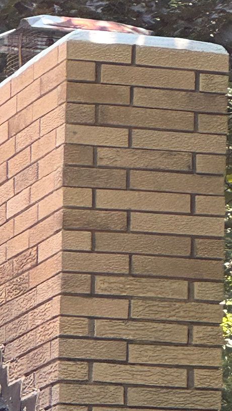 Tall brick chimney with a metal cap, featuring light-colored rectangular bricks in a vertical pattern.