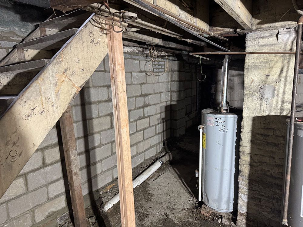 Basement with stairs, cinder block walls, and a water heater. Wooden beams and pipes are visible.