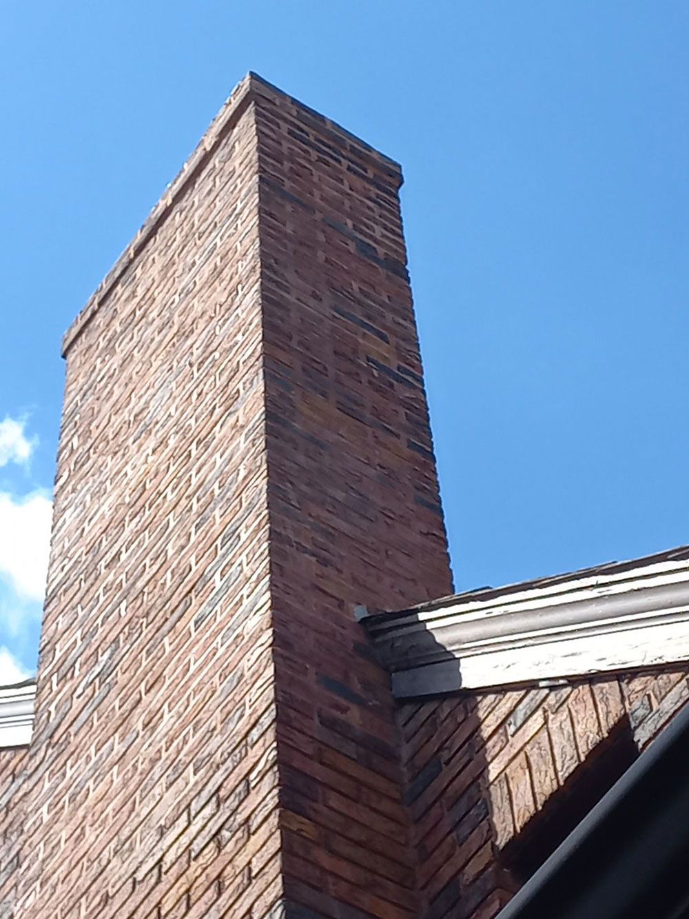 Tall brick chimney against a clear blue sky, standing on a building with white trim.