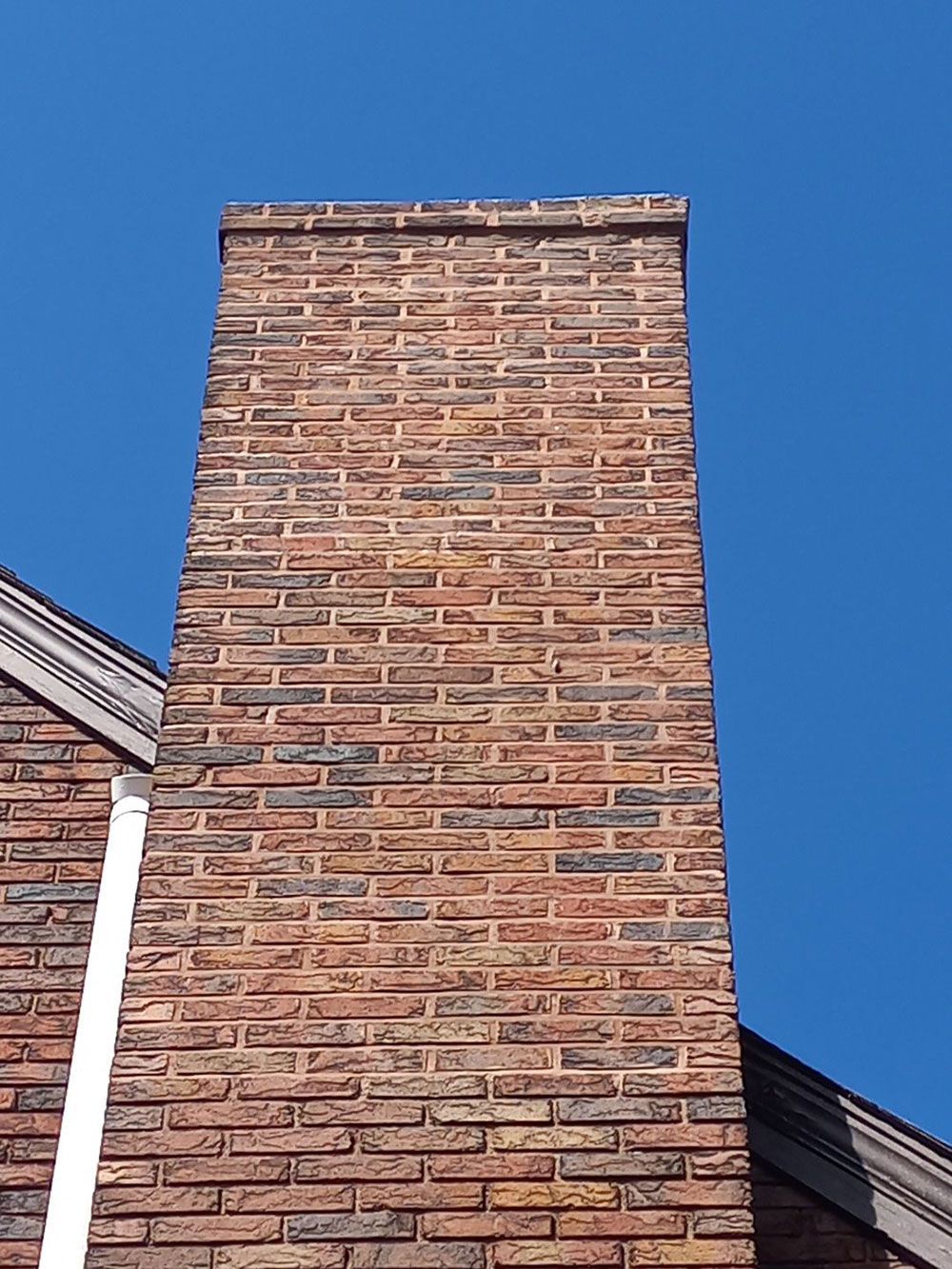 Tall brick chimney against a bright blue sky. The brick is primarily red-brown with some darker accents.