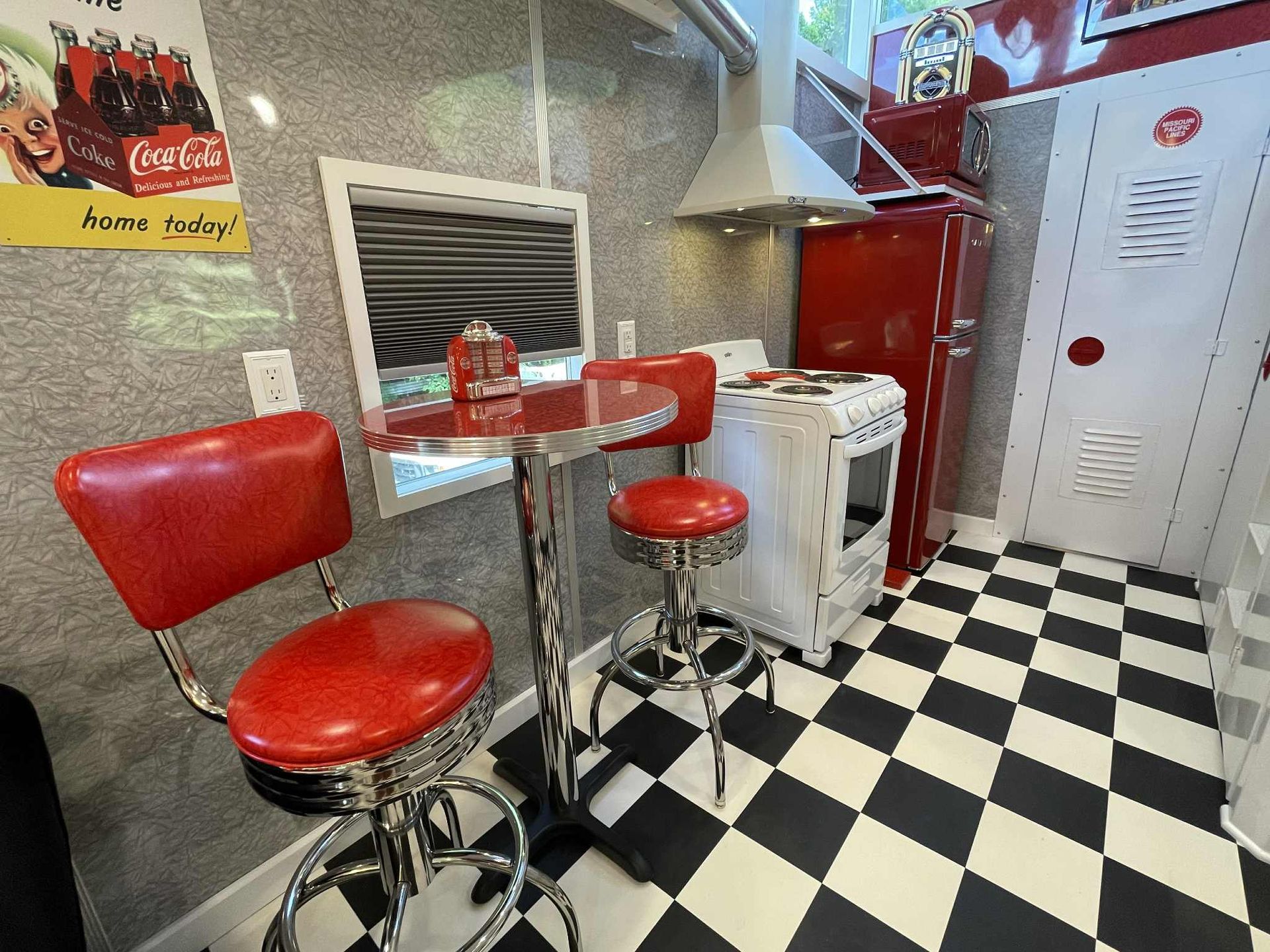 Retro diner-style kitchen with red chairs, a small table, a red refrigerator, and black-and-white checkered floor.