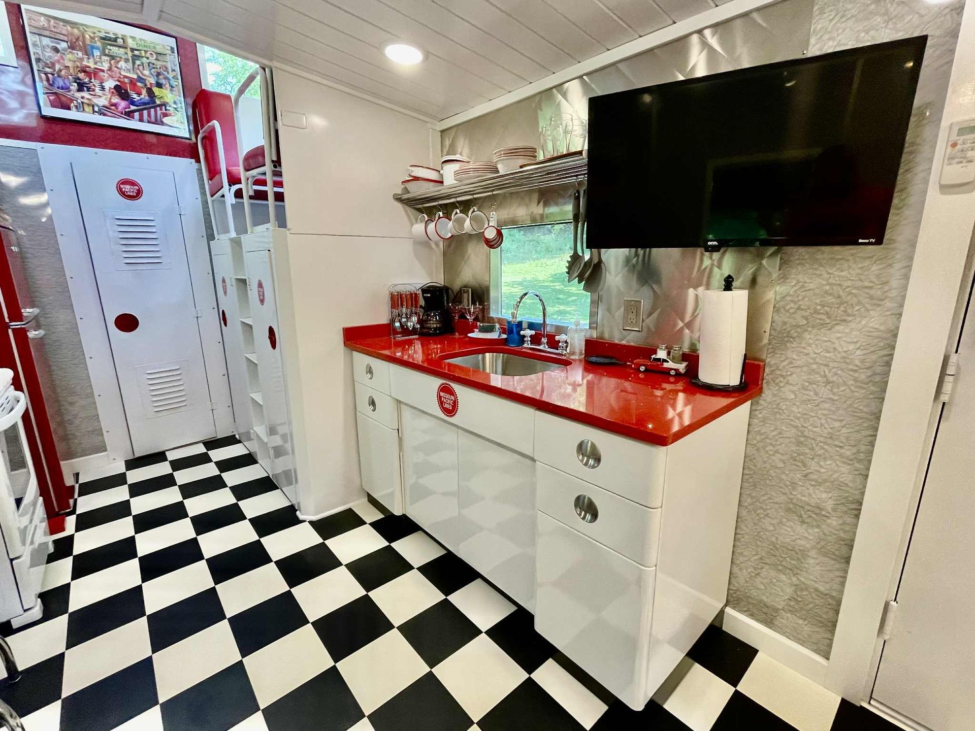 Diner-style kitchenette with red countertop, stainless steel appliances, black and white checkered floor