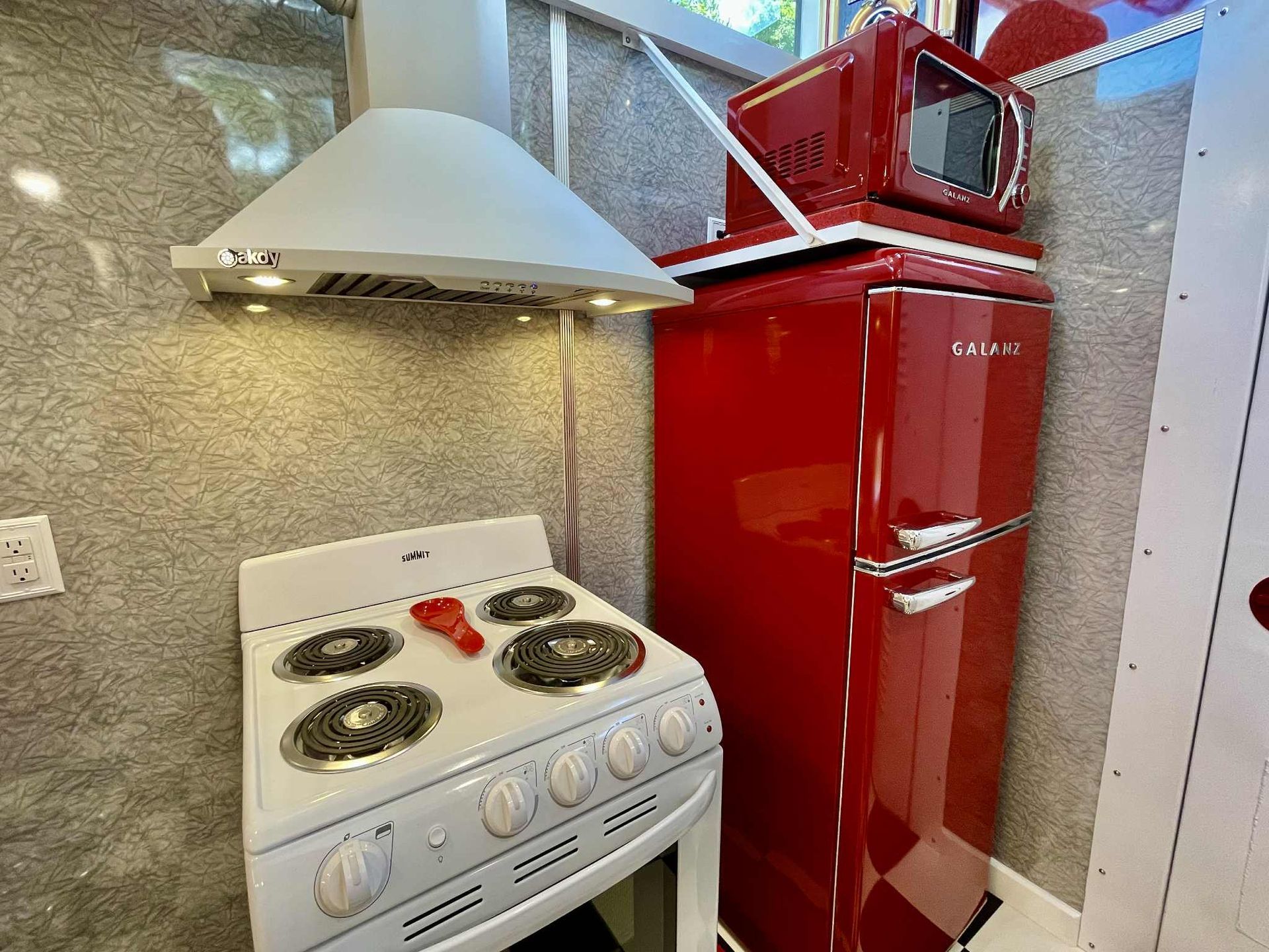White stove, range hood, and red refrigerator with microwave in a small kitchen.