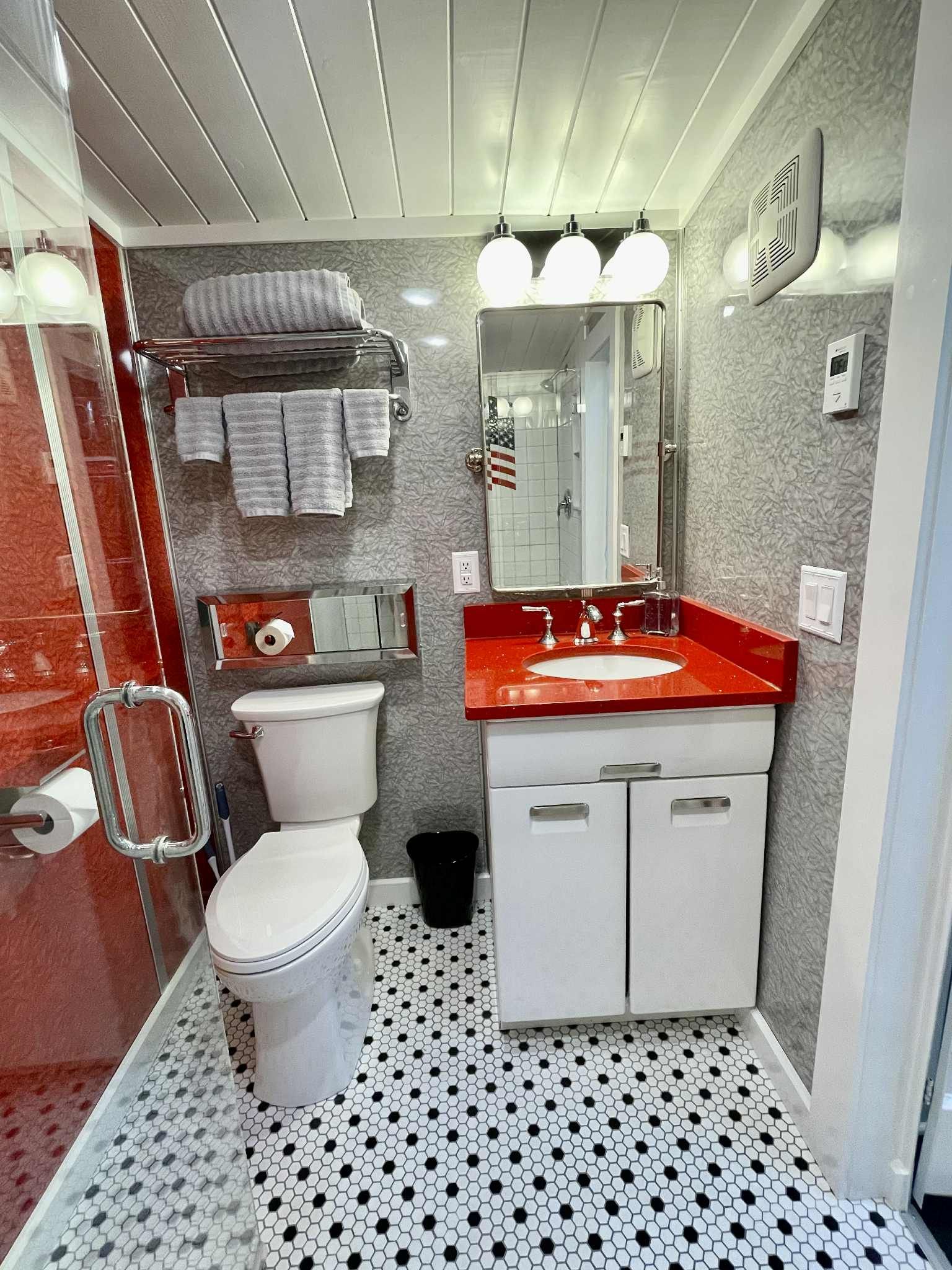 Small bathroom with red accents: white toilet, sink, countertop, and tiled floors.