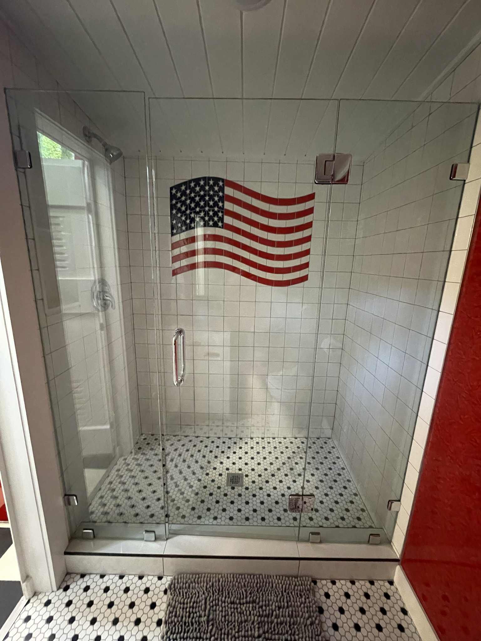 Glass shower with an American flag decal on white subway tile. Black and white patterned floor.
