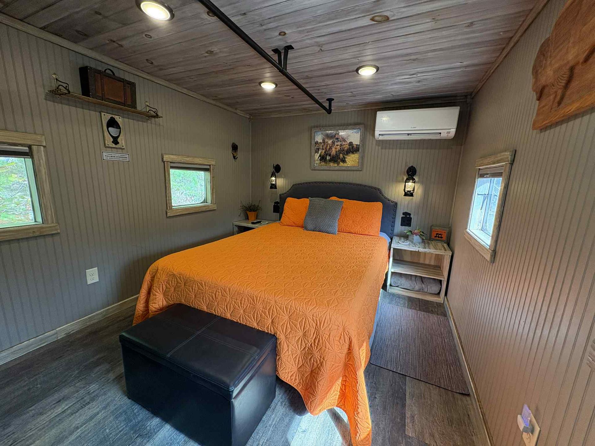 Bedroom with orange bedding, small windows, and wood accents.