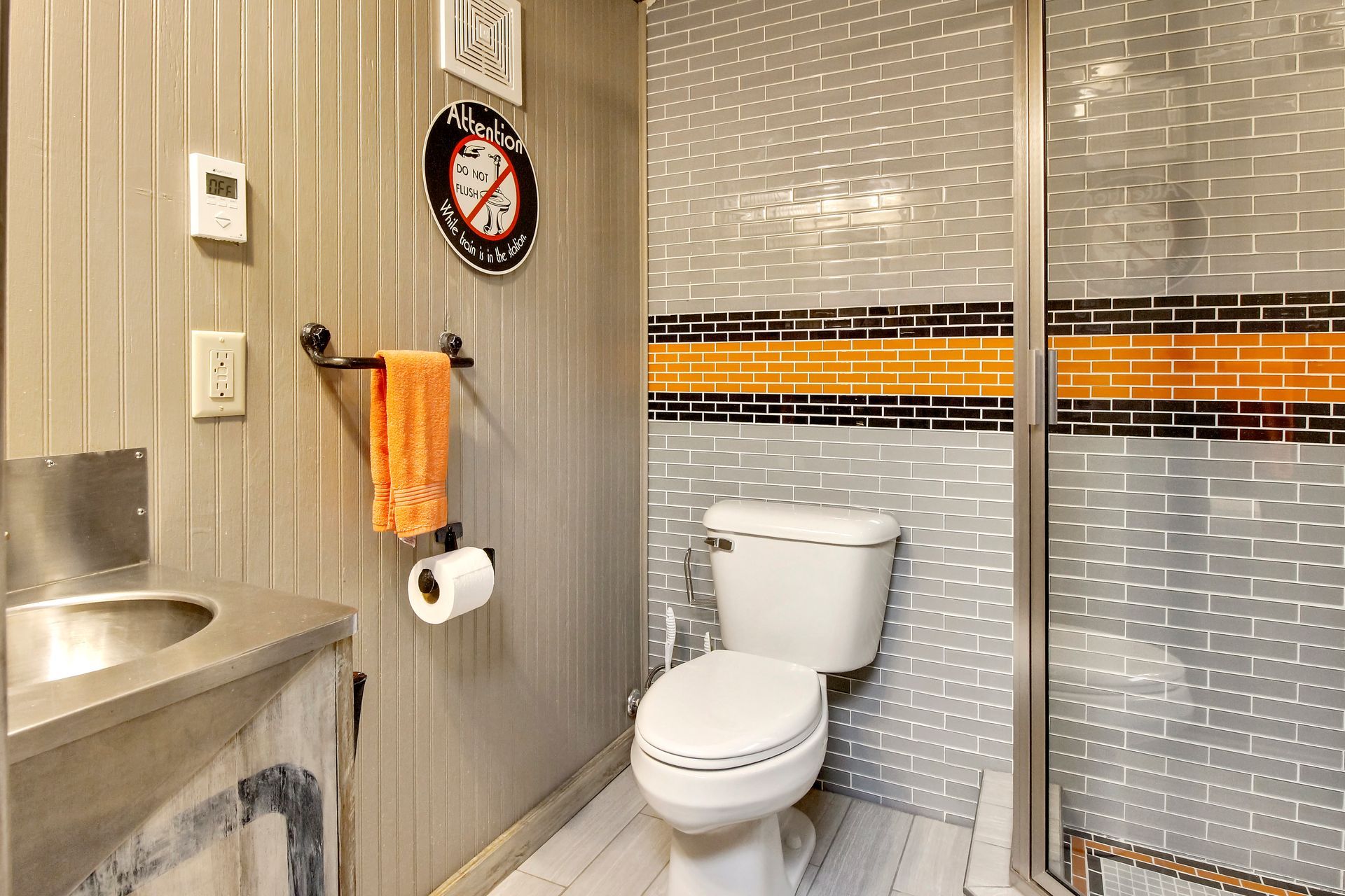 Bathroom with gray paneling, patterned tiled walls, toilet, and a walk-in shower.