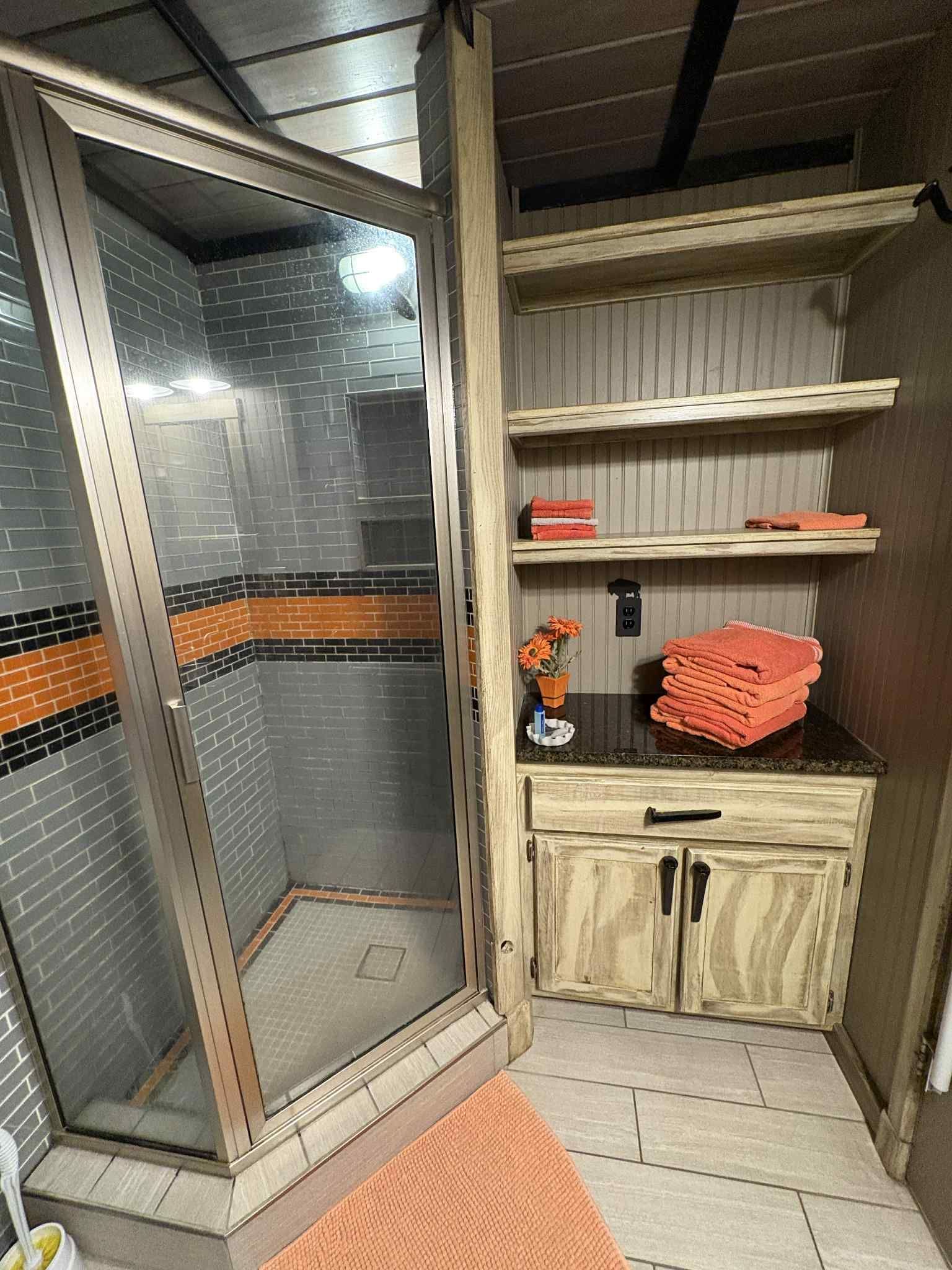Bathroom with a glass shower, shelves, and a vanity. Orange and white color scheme.