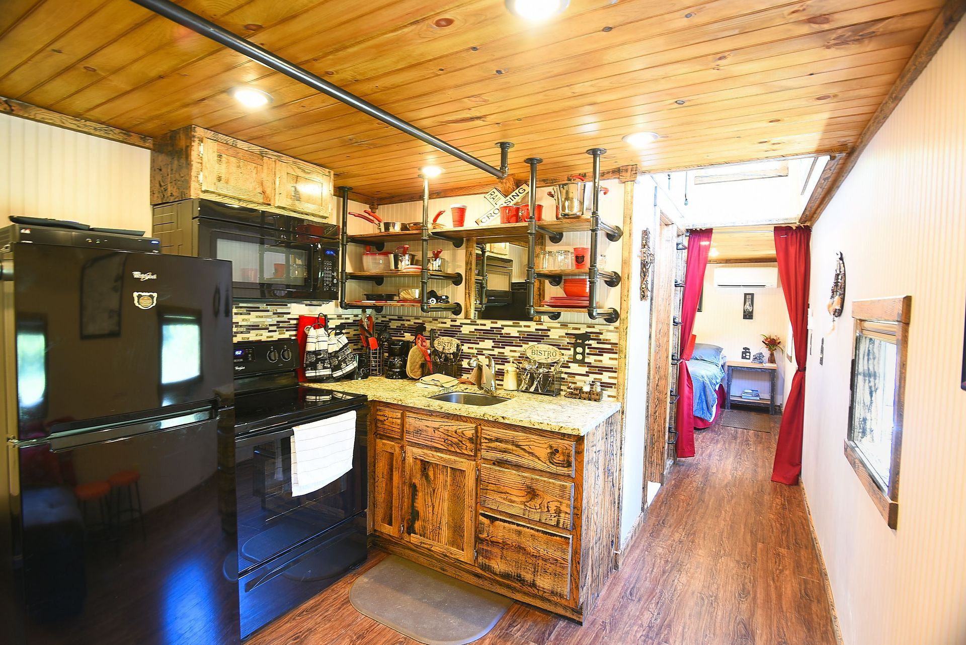 Kitchen interior with wooden cabinets, shelving, and appliances, leading into a hallway.
