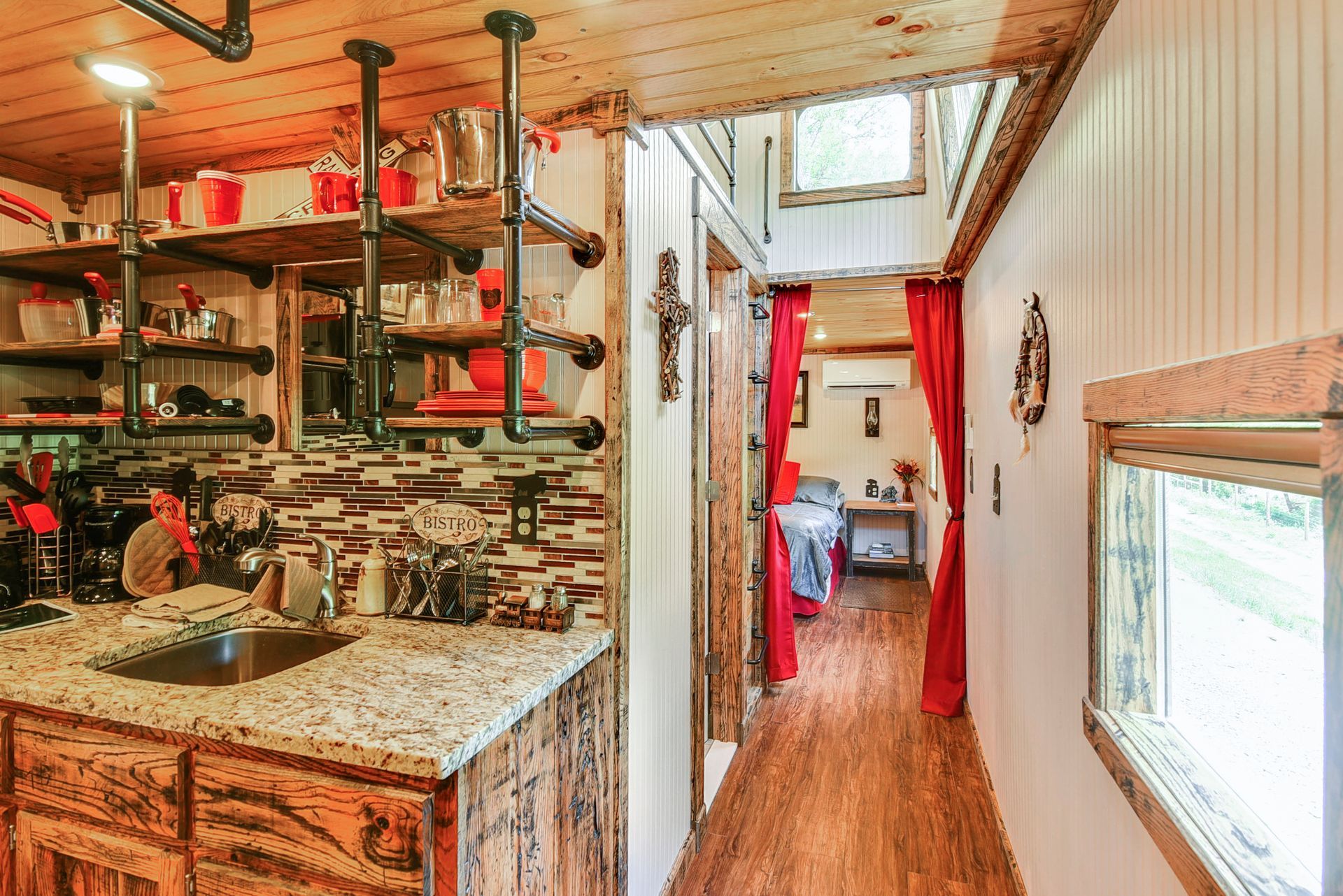 Tiny home interior with a kitchen, hallway, and living area with red curtains.