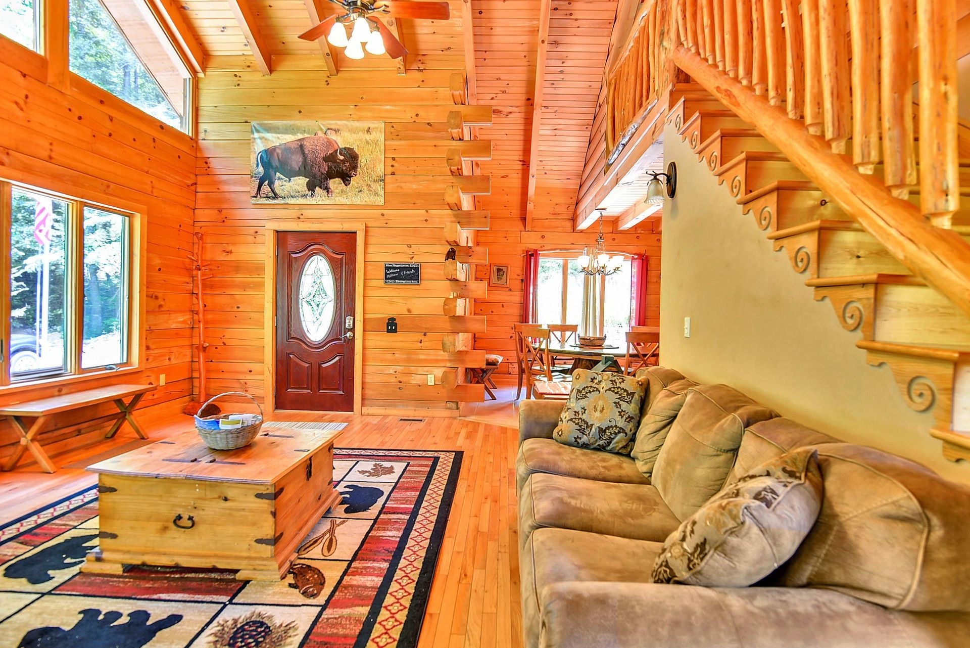 Cozy log cabin interior with wooden walls and furniture, a staircase, and a sofa.