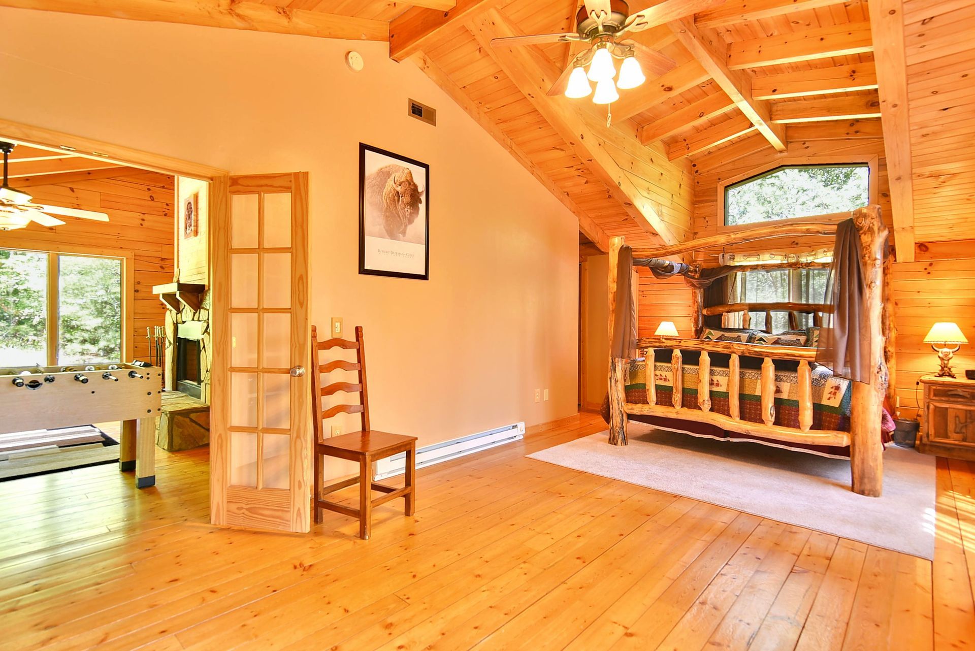 Wooden bedroom with a four-poster bed, wood floors, and a view into a game room.