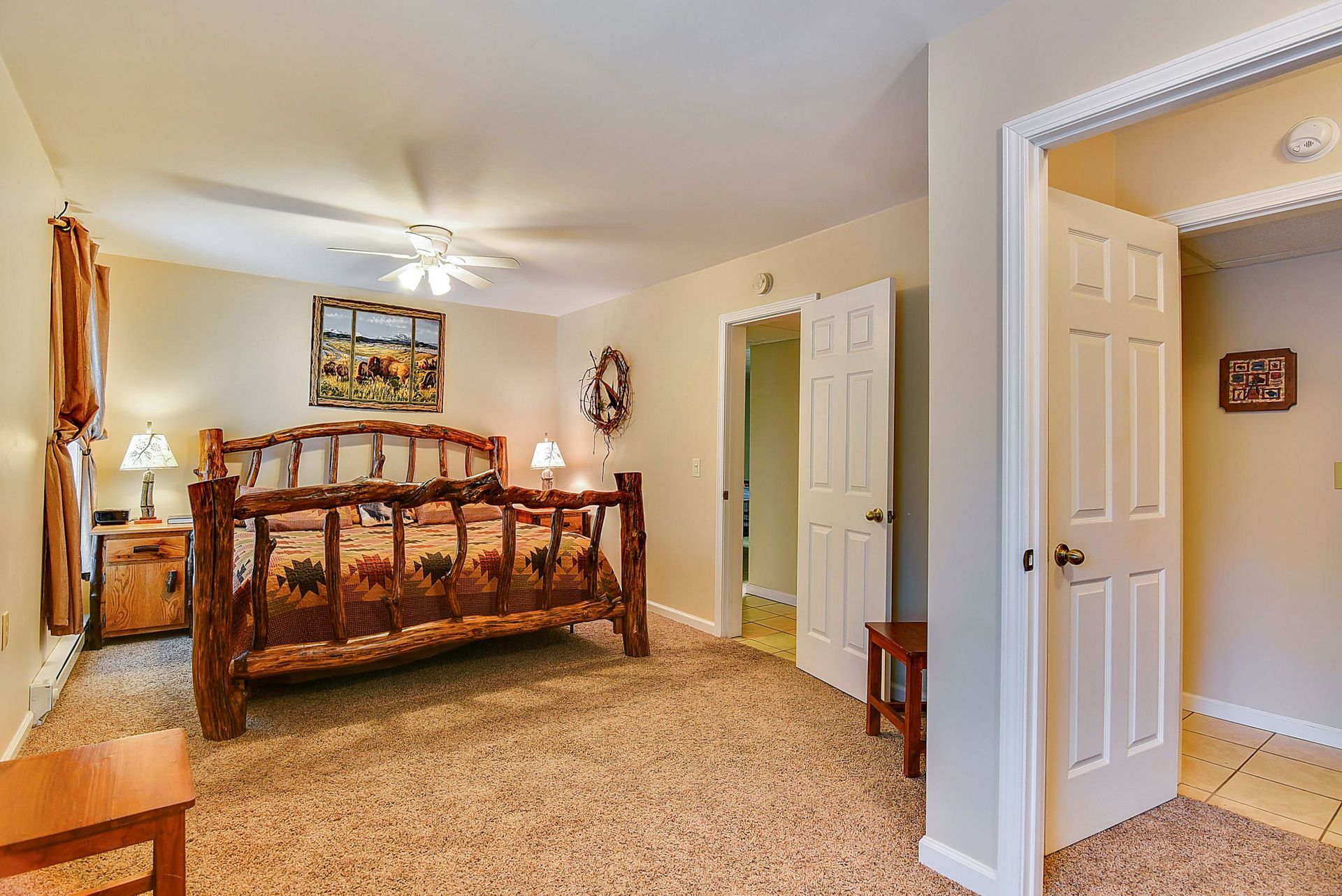 Bedroom with rustic wooden bed, carpet, open doorways to a bathroom and another room.
