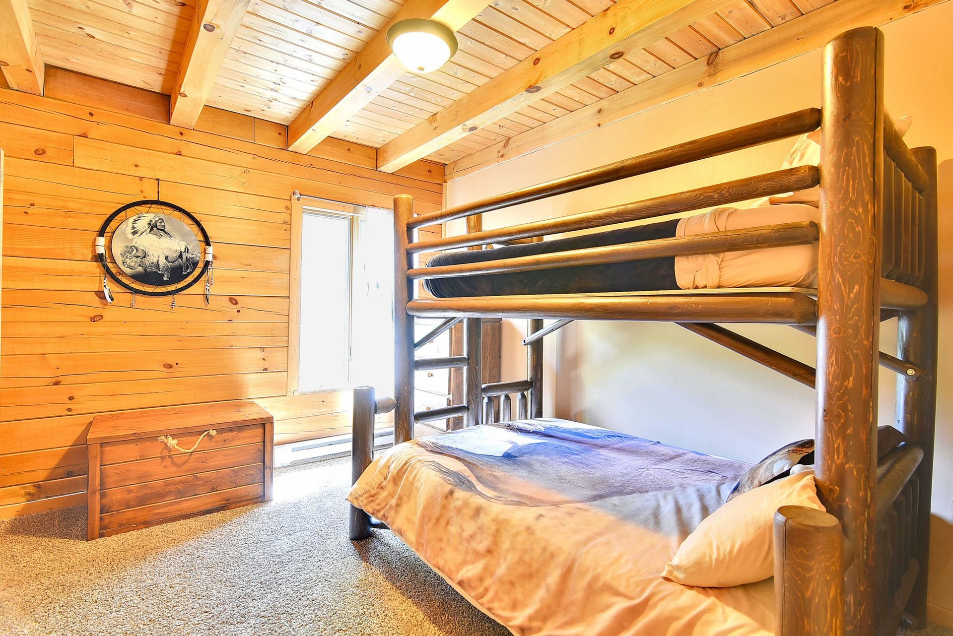 Bedroom with wooden bunk beds, wooden walls, chest, and a porthole-style wall decoration.