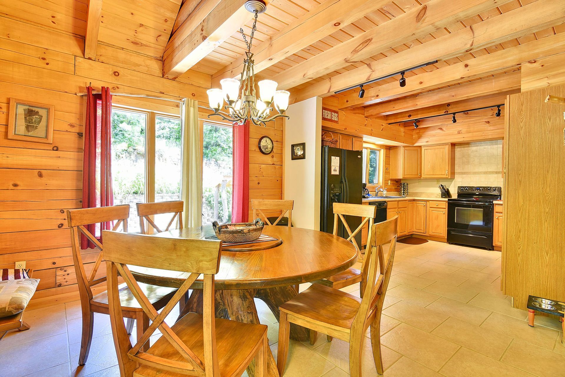 Dining area in a log cabin with a round table, wooden chairs, and kitchen in the background.