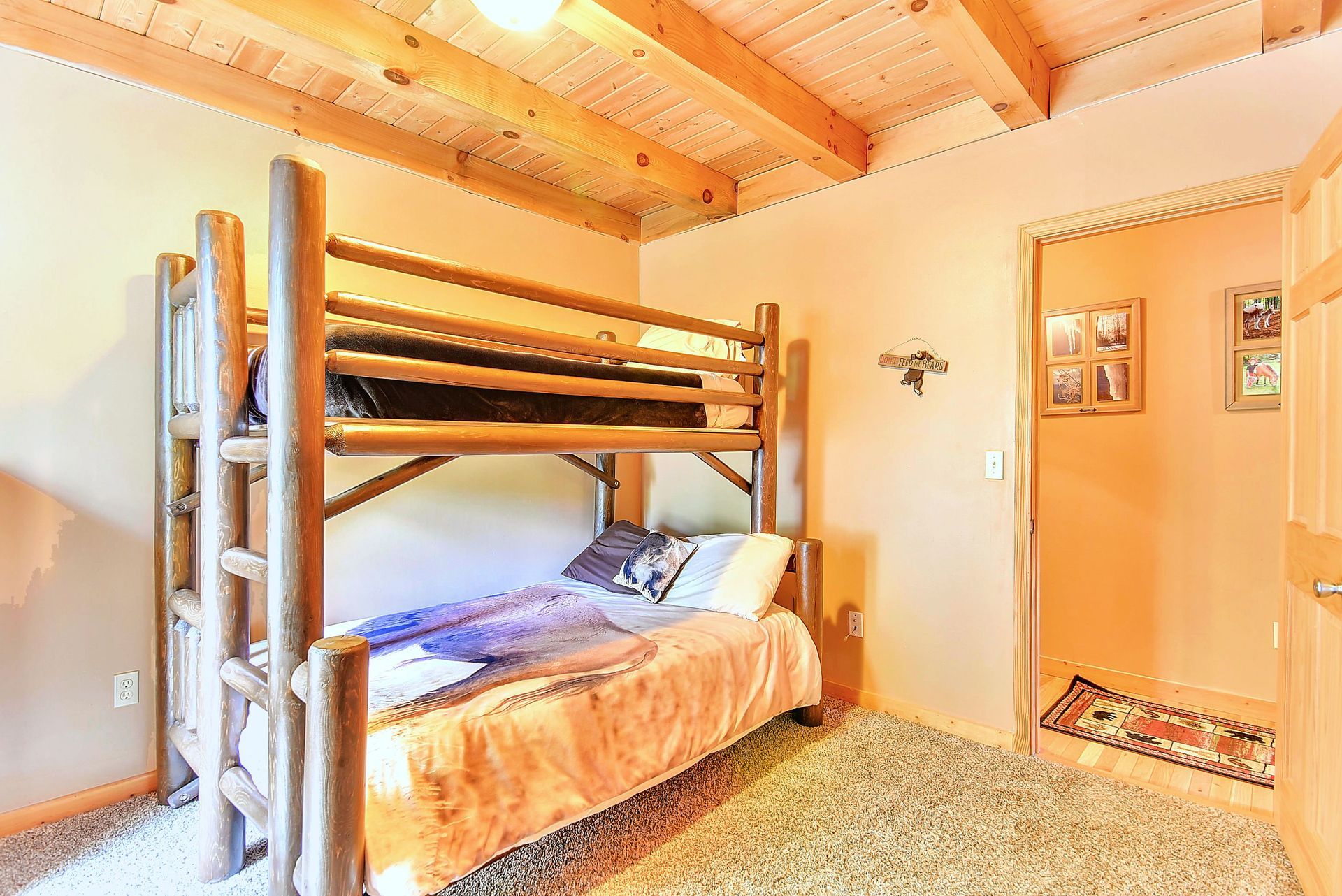 Bunk beds in a rustic bedroom with wood beams, peach walls, and carpet. Doorway visible to right.