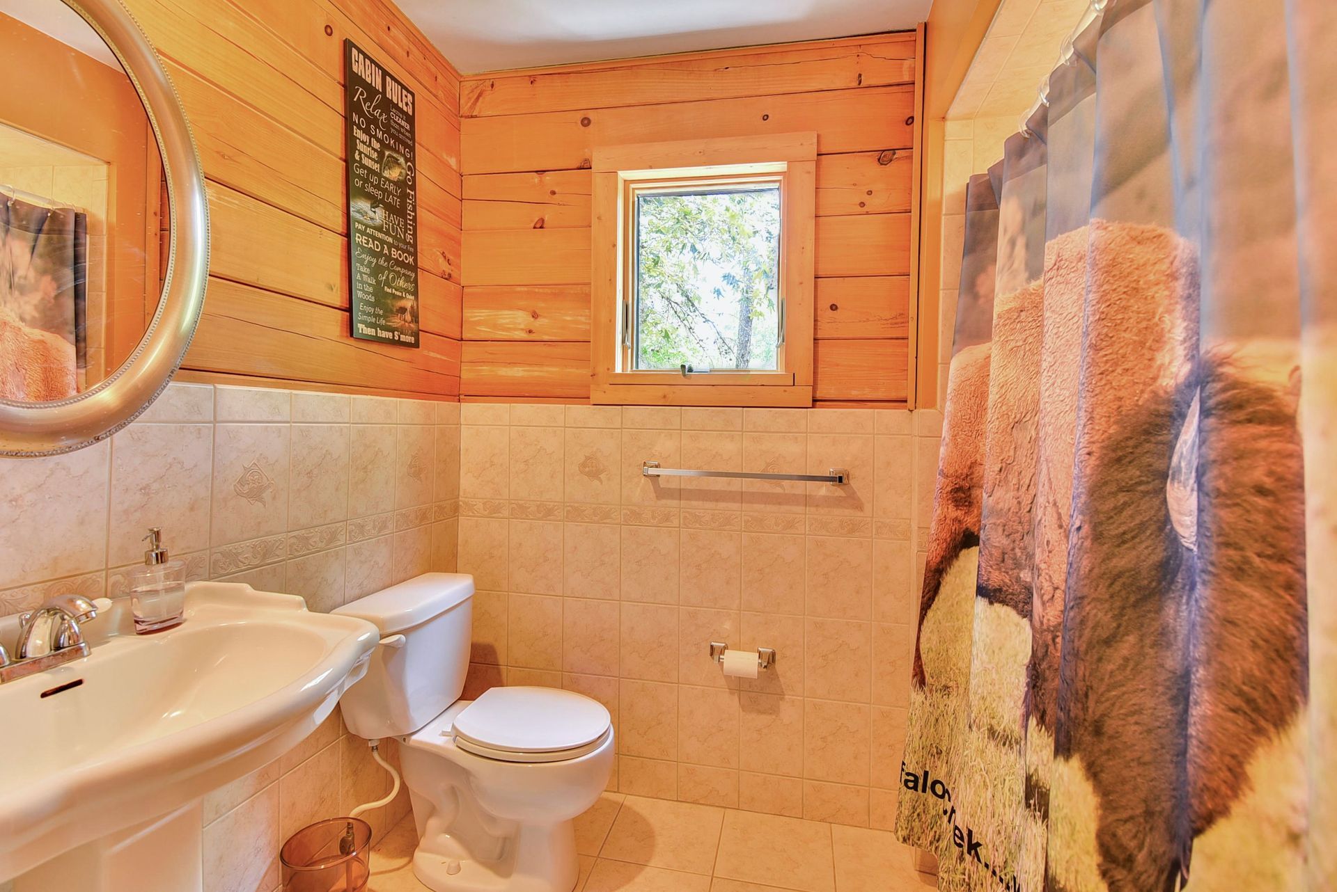 Bathroom with wooden walls and beige tile. A toilet, sink, and cow-print shower curtain are visible.