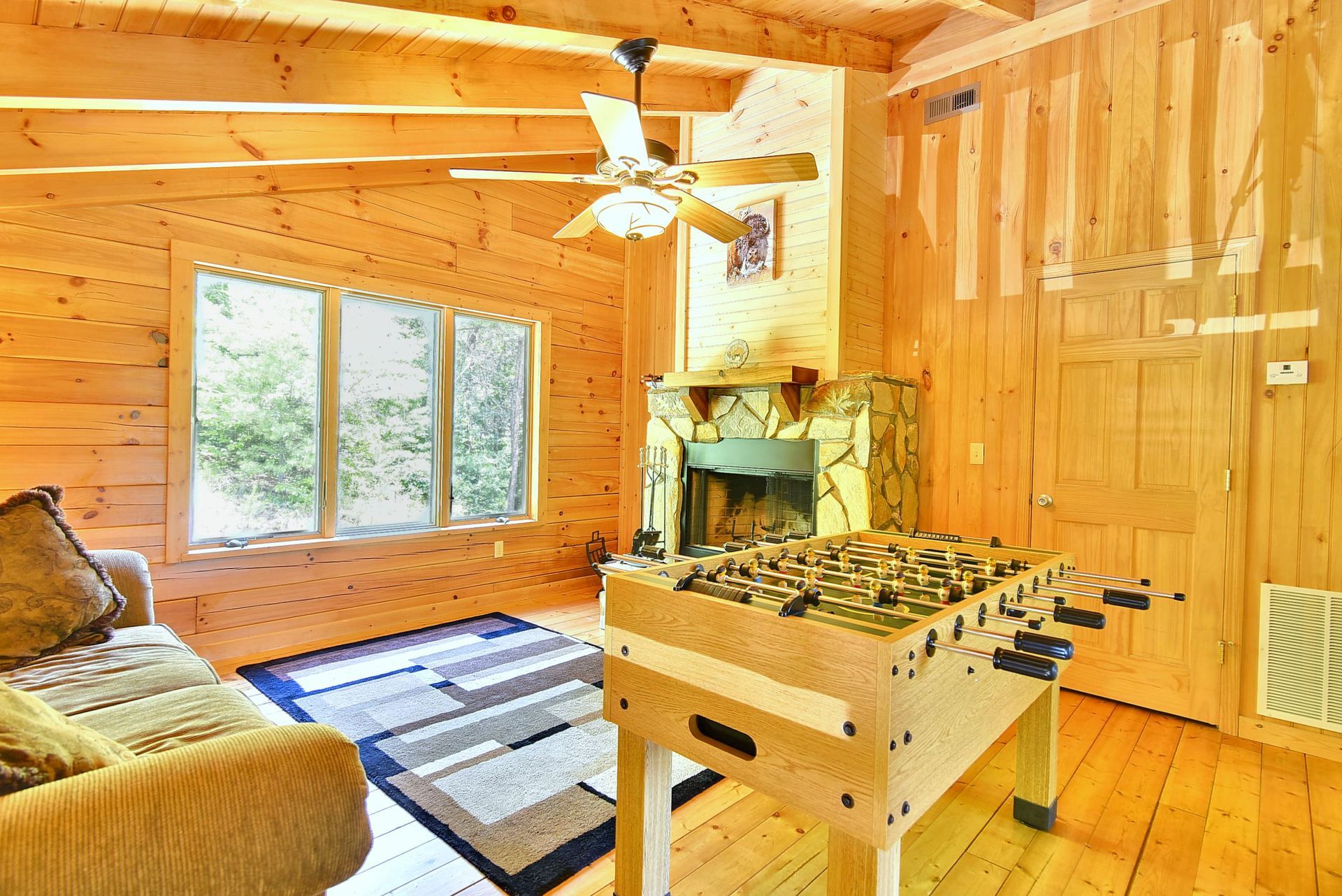 Wooden cabin living room with foosball table, fireplace, couch, and large windows.
