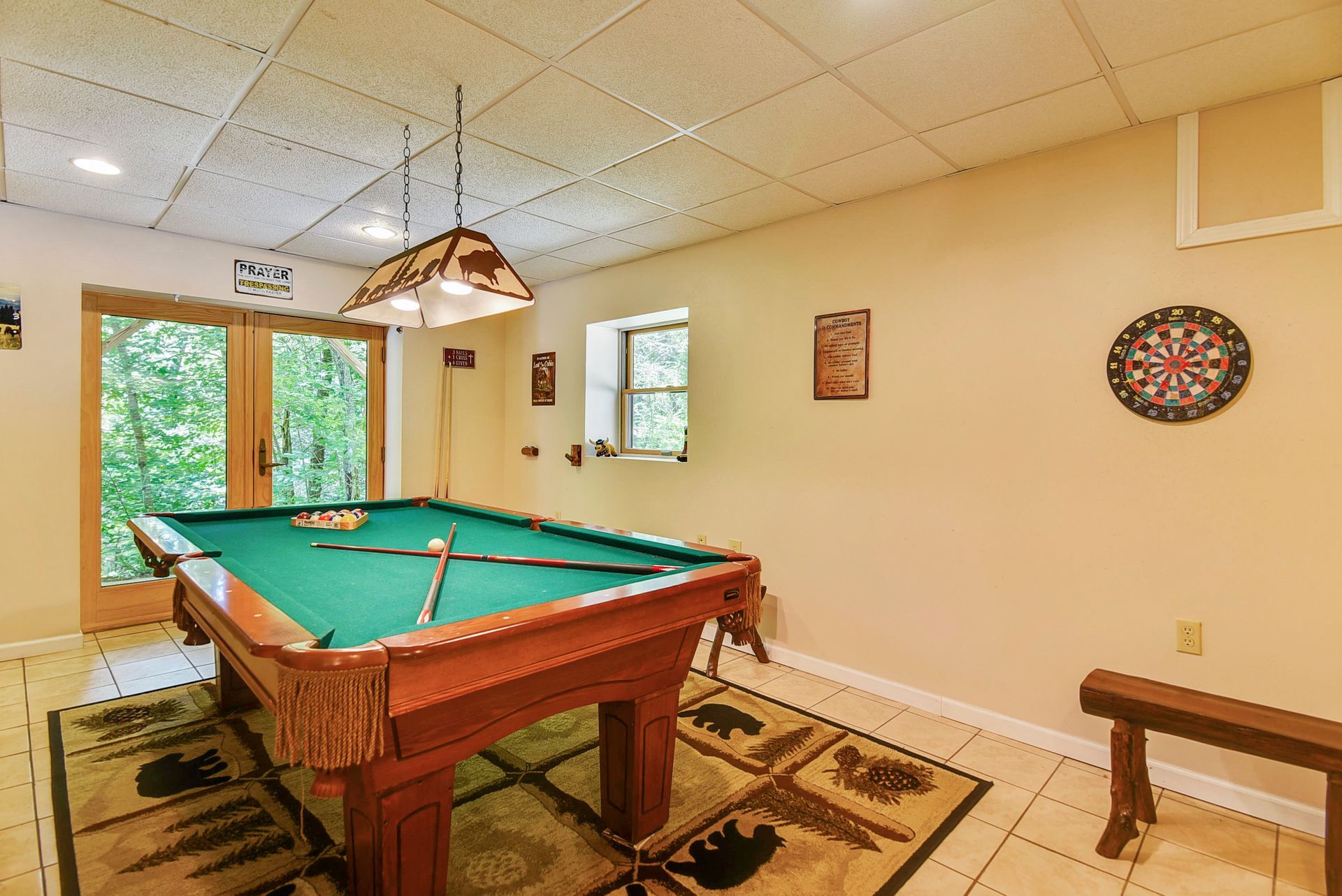 Pool table in a game room with forest view, wood accents, and dartboard.
