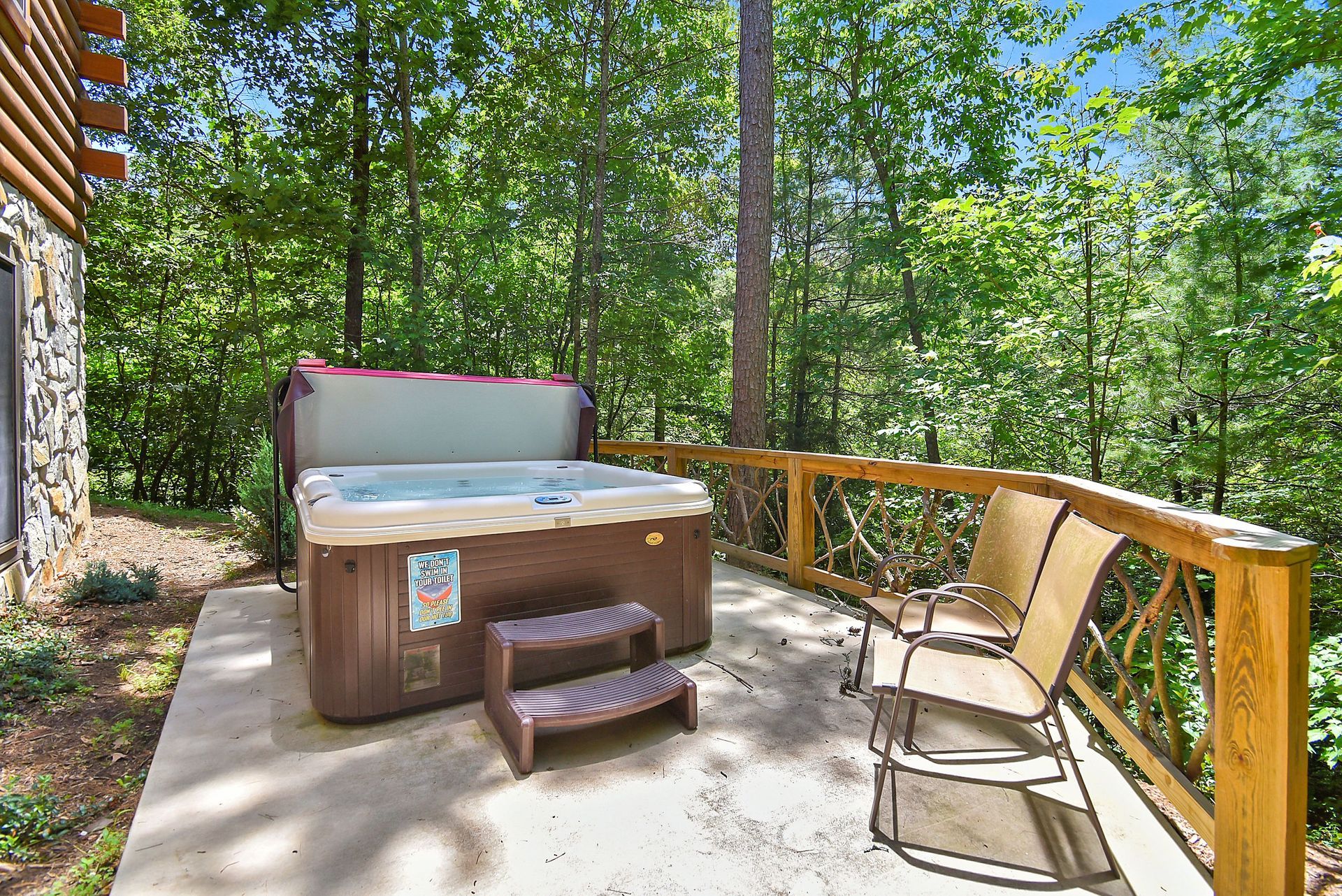 Hot tub on a wooden deck surrounded by trees. Two chairs are next to the railing.