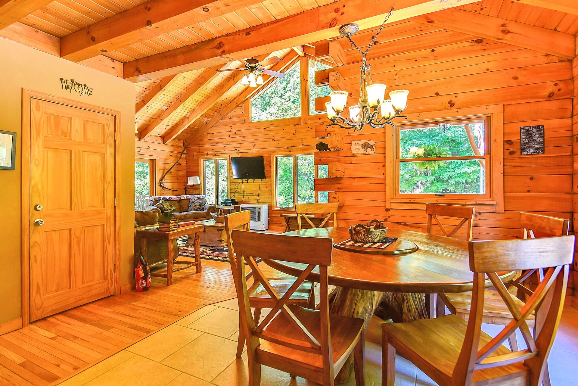 Wooden dining room with round table and chairs, visible windows and a chandelier.