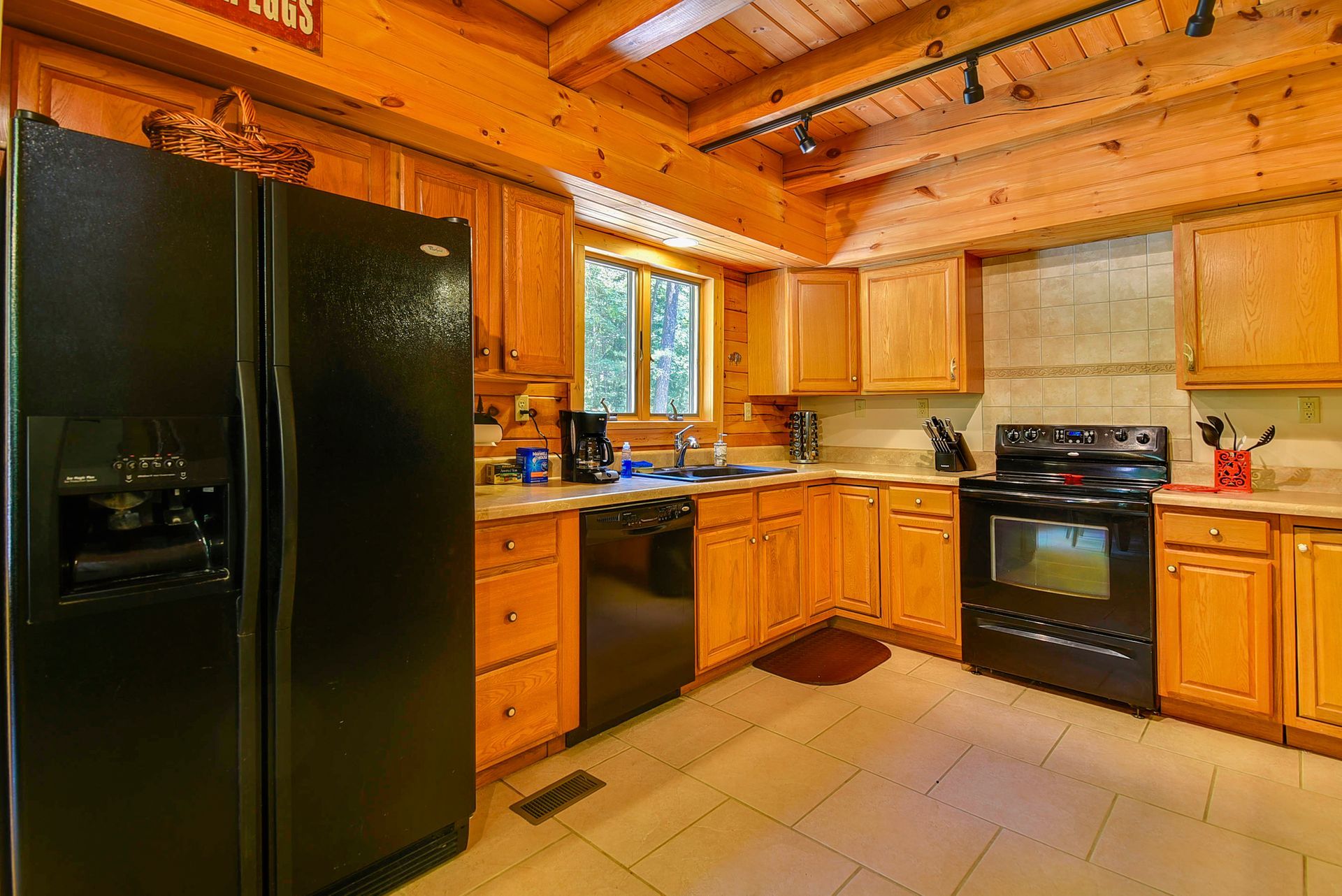 Kitchen with black appliances, light wood cabinets, and beige countertops and flooring.
