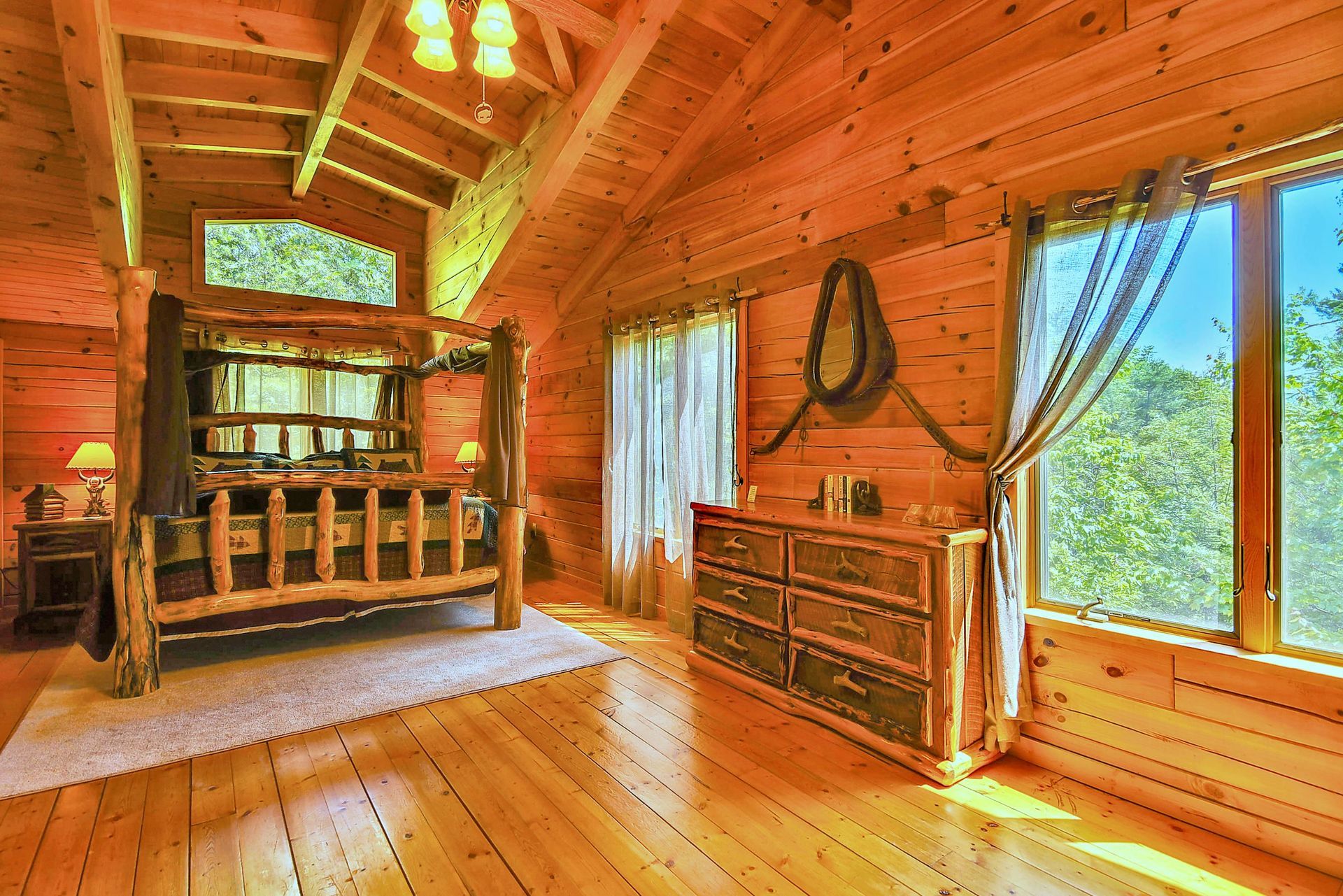 Wooden bedroom with a four-poster bed, dresser, windows, and exposed beams, creating a cozy cabin atmosphere.