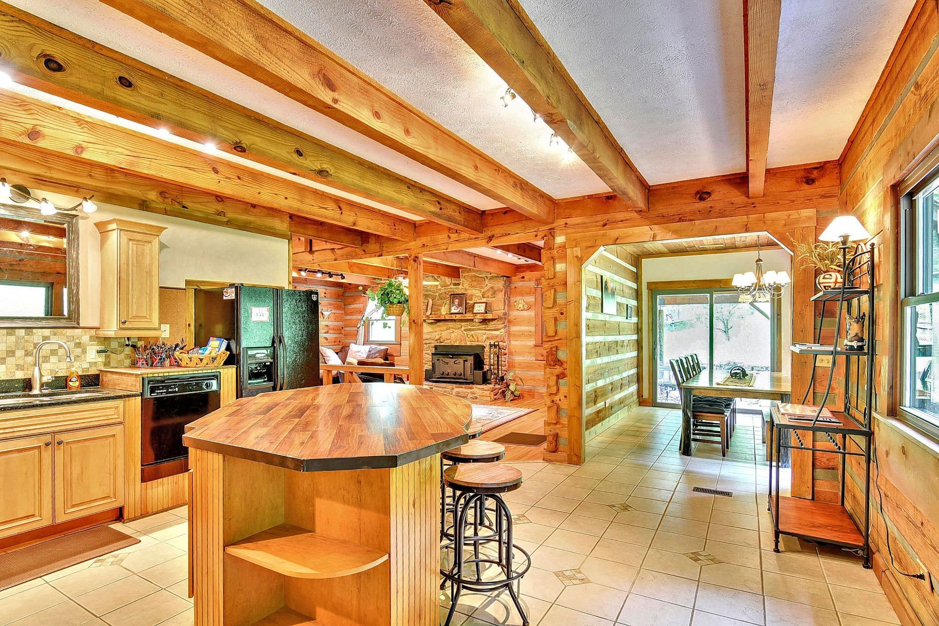 Spacious wood-paneled kitchen with island and bar stools, leading to dining area and fireplace.
