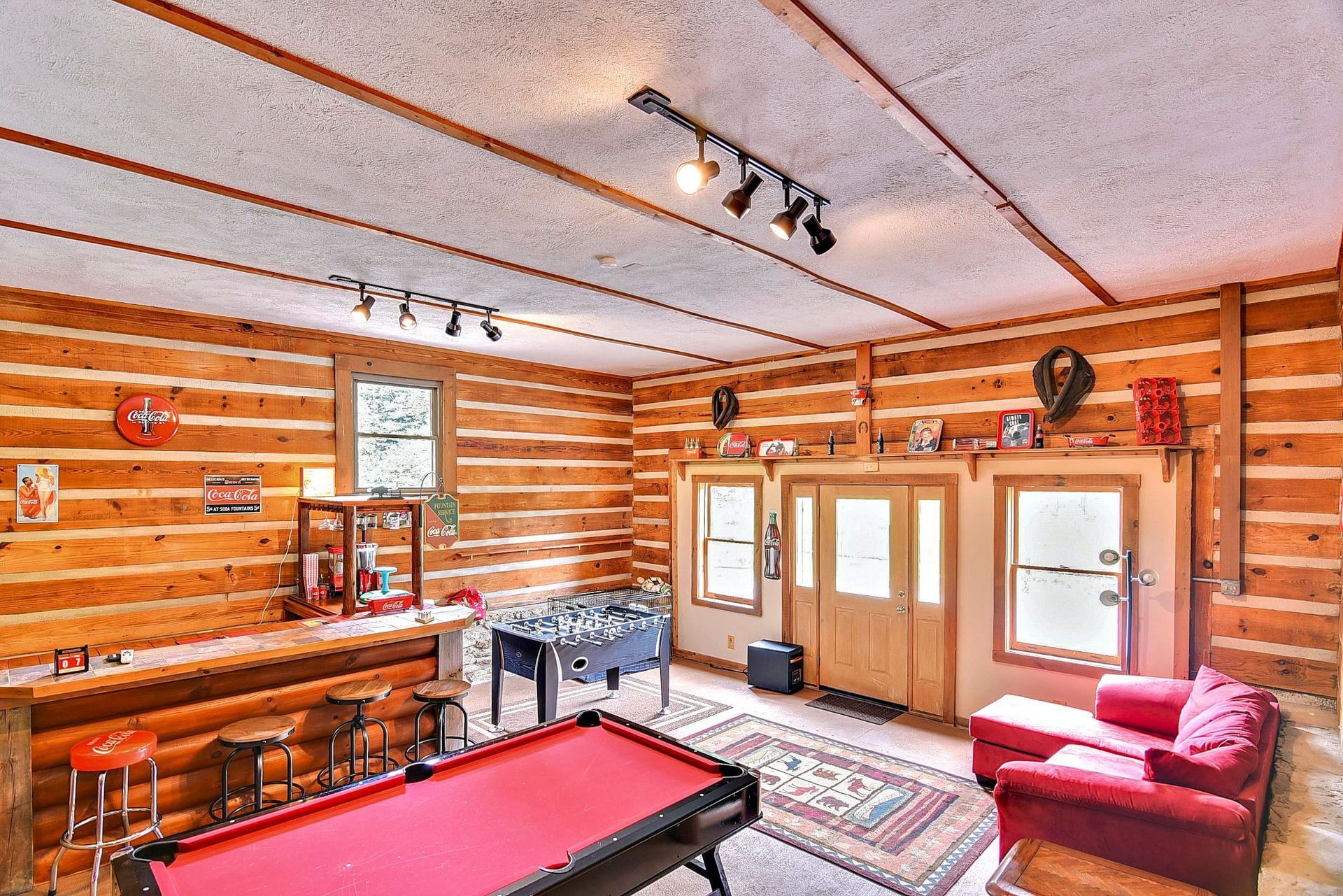 Recreation room with log walls: red pool table, foosball, bar, red sofa, and door.