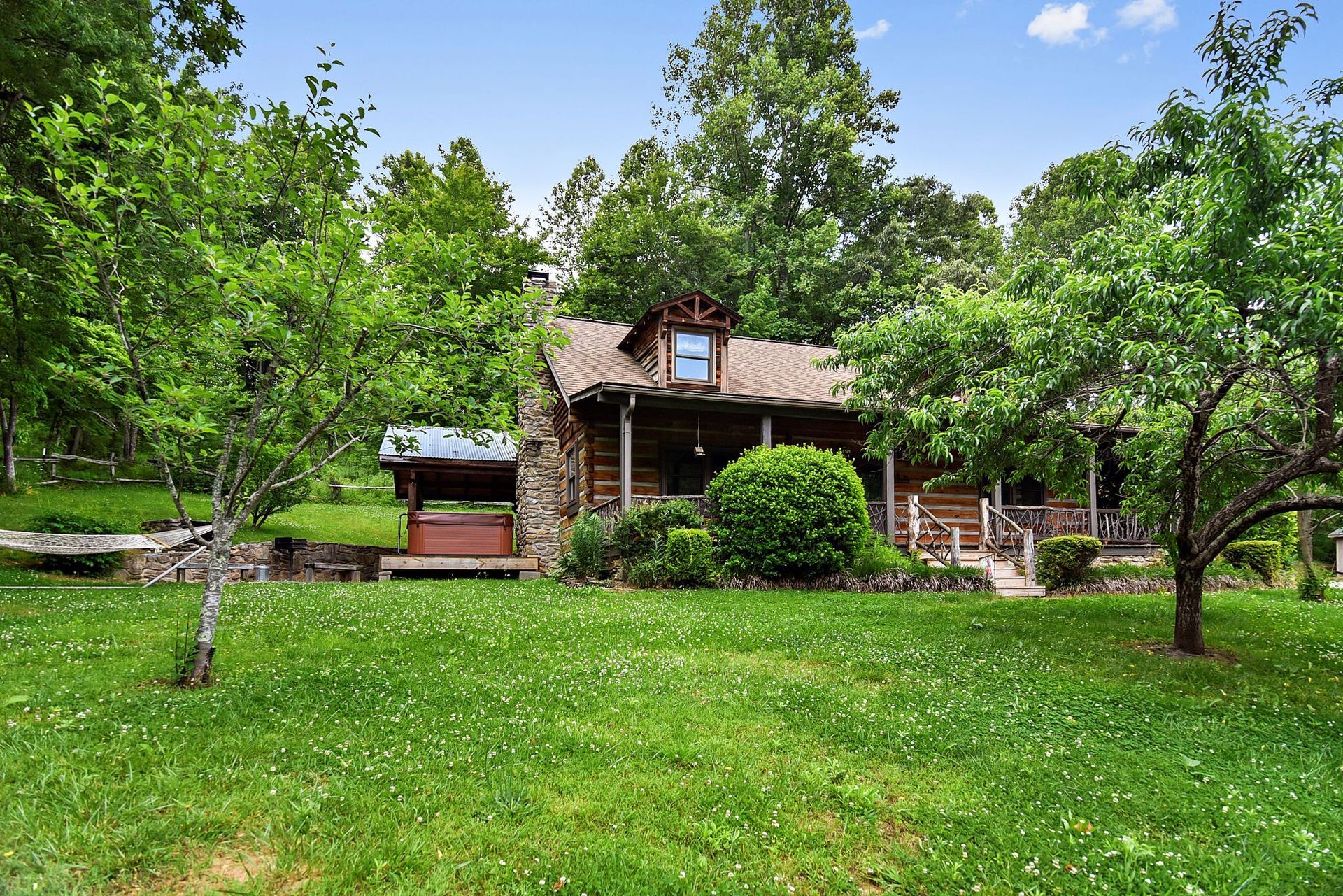 Log cabin surrounded by green grass and trees under a blue sky.