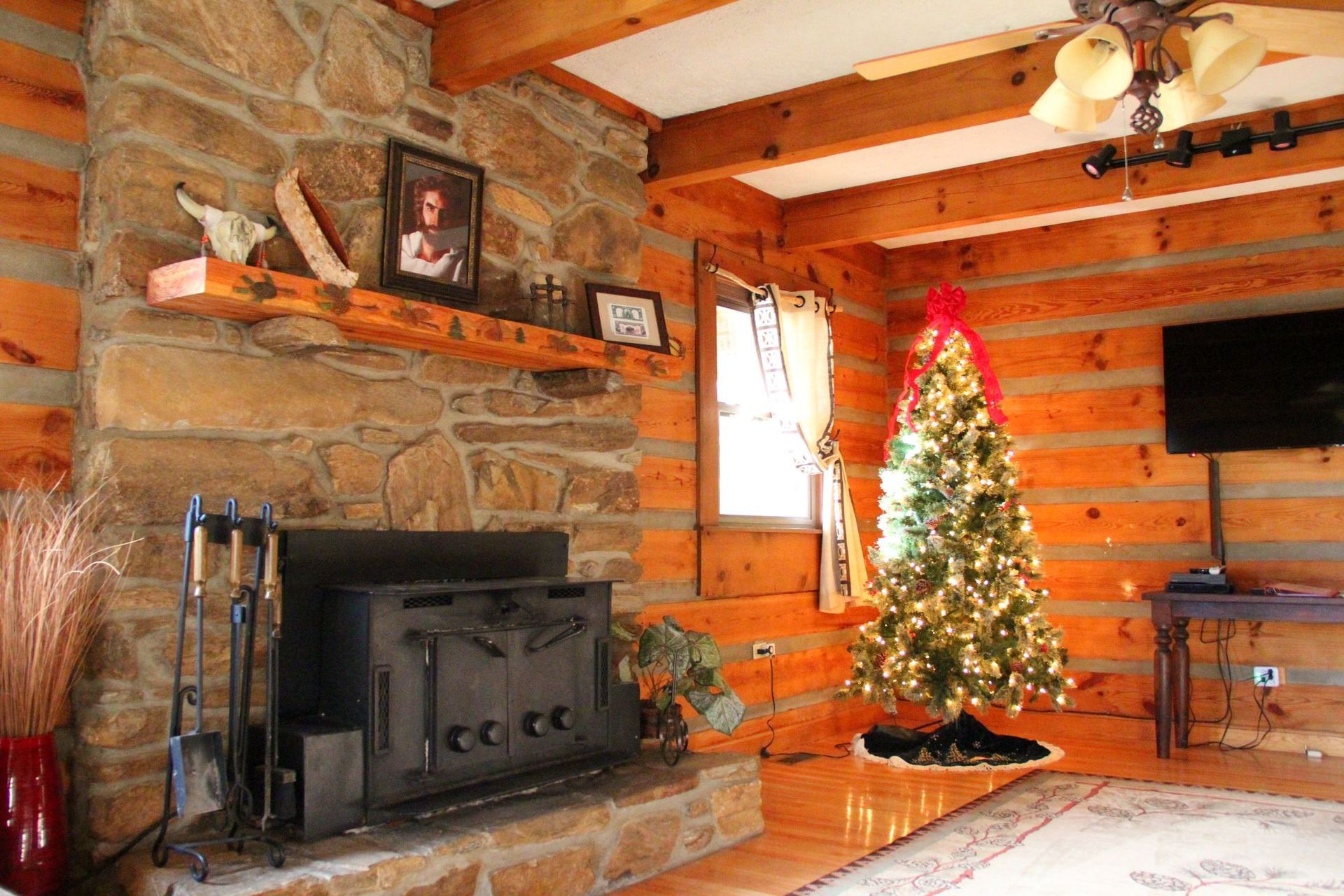 Log cabin living room with stone fireplace, Christmas tree, and wood paneling.