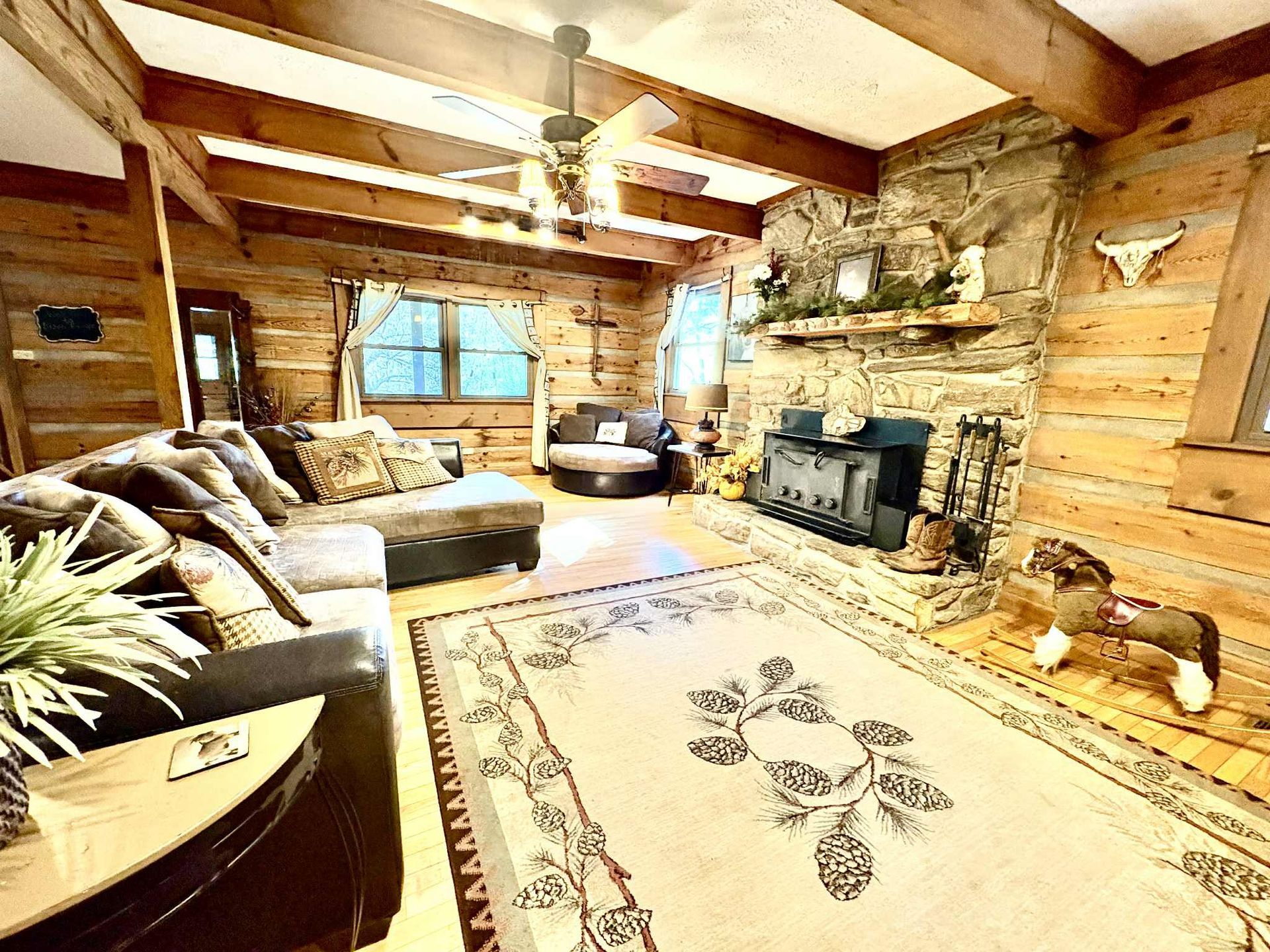 Cozy cabin living room with a stone fireplace, log walls, and a patterned rug.