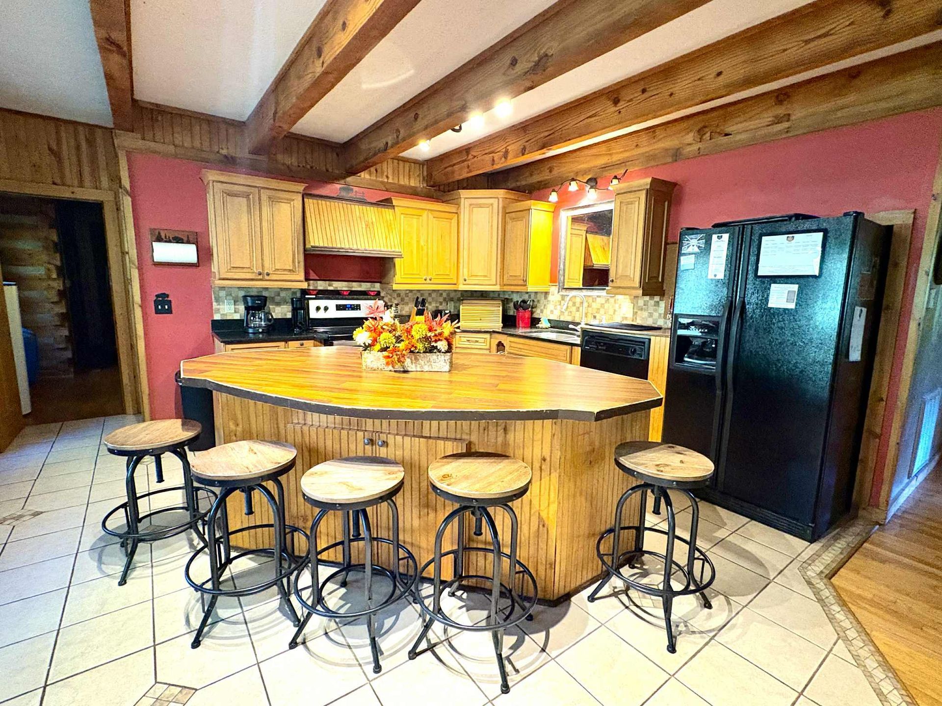 Kitchen with wood cabinets, island, and bar stools; black appliances and pink walls.