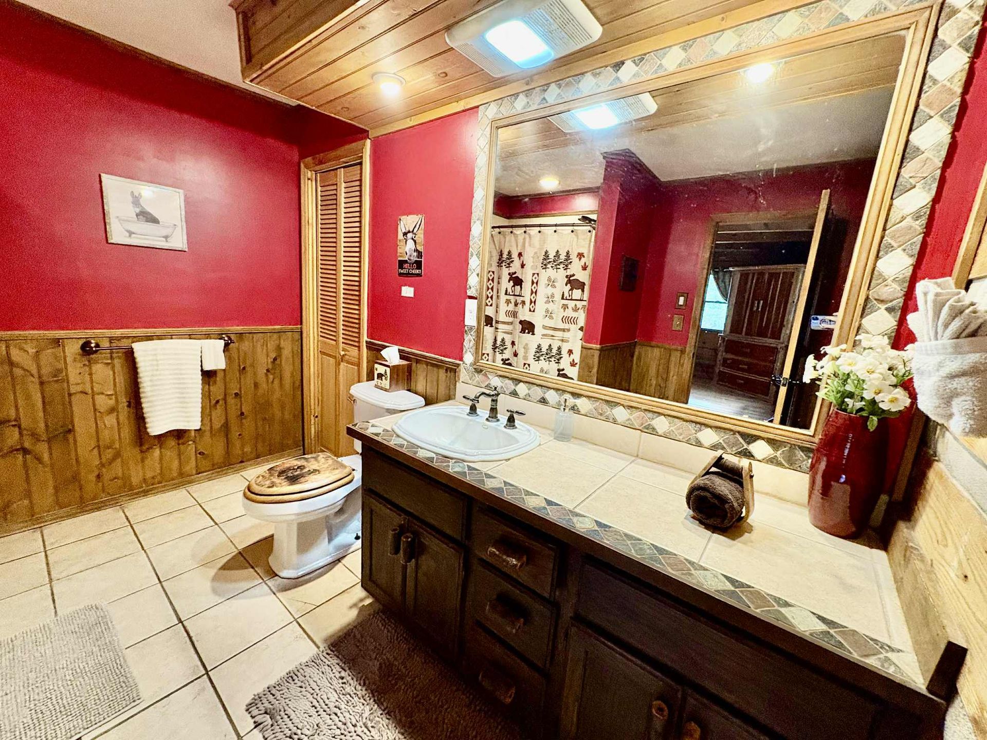 Rustic bathroom with red walls, wooden paneling, and large mirror.