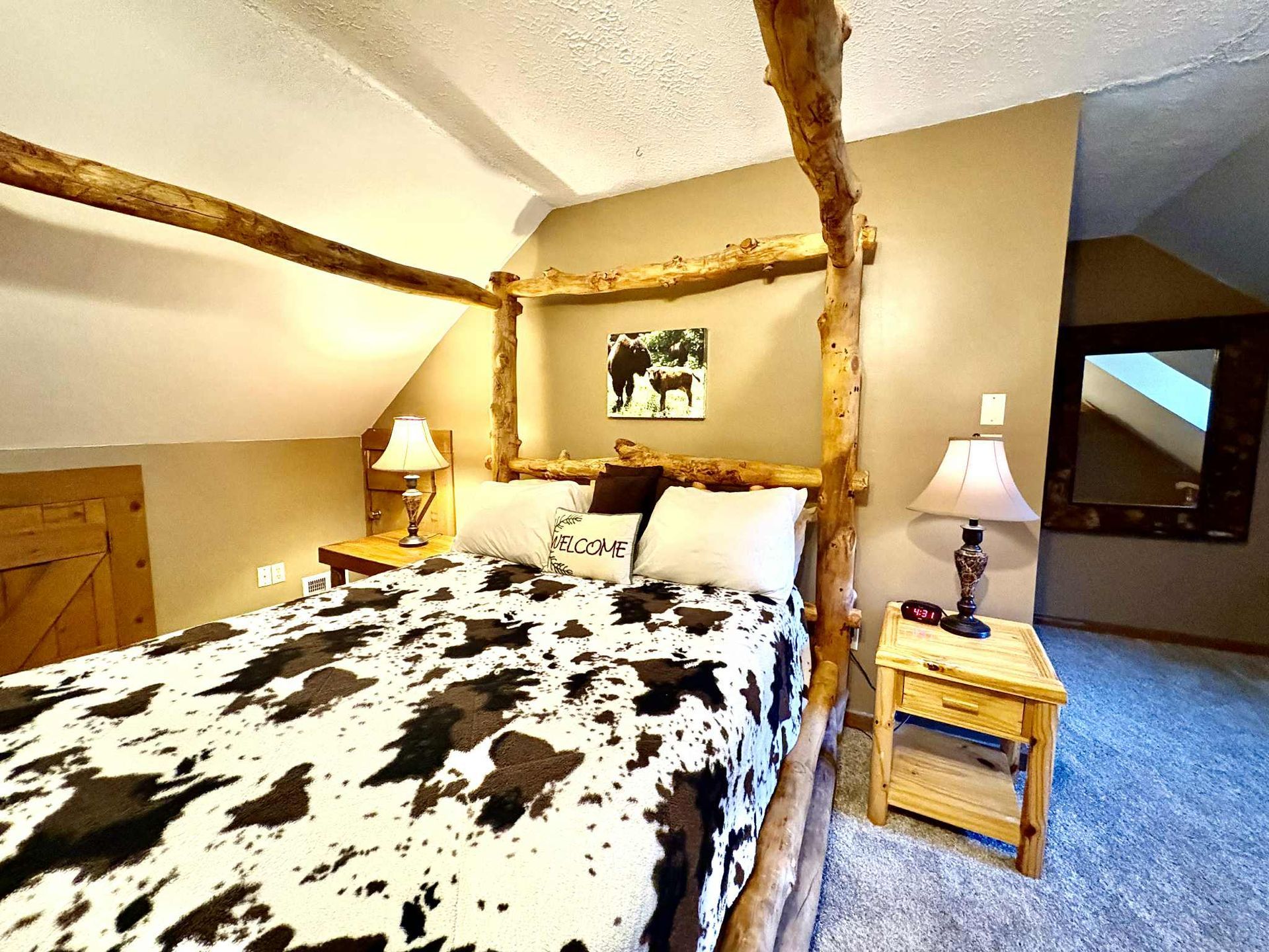 Bedroom with a rustic log bed frame, cowhide patterned bedding, and two nightstands.