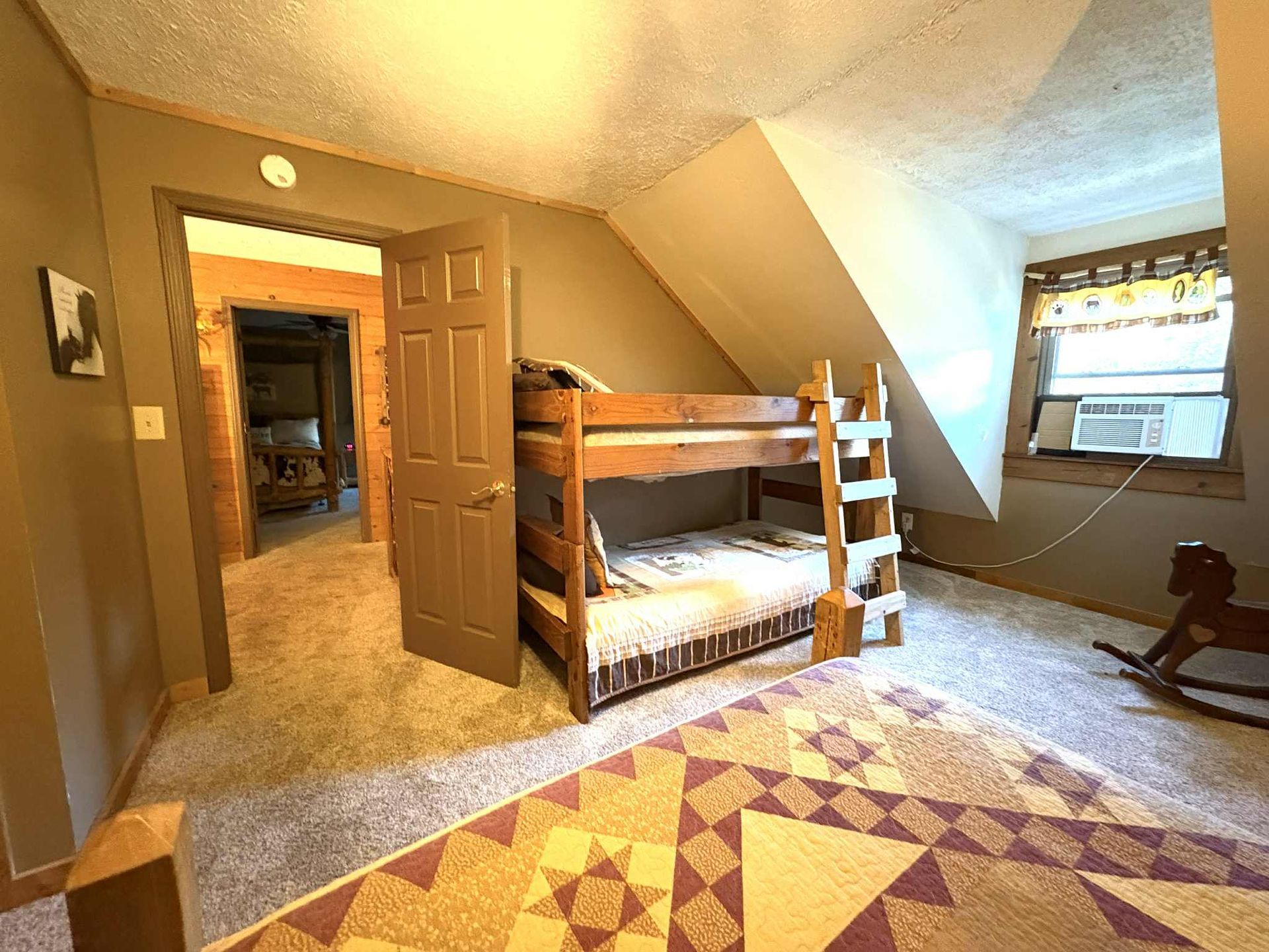 Bunk beds in a room with a patterned rug, door to another room, and a small window.