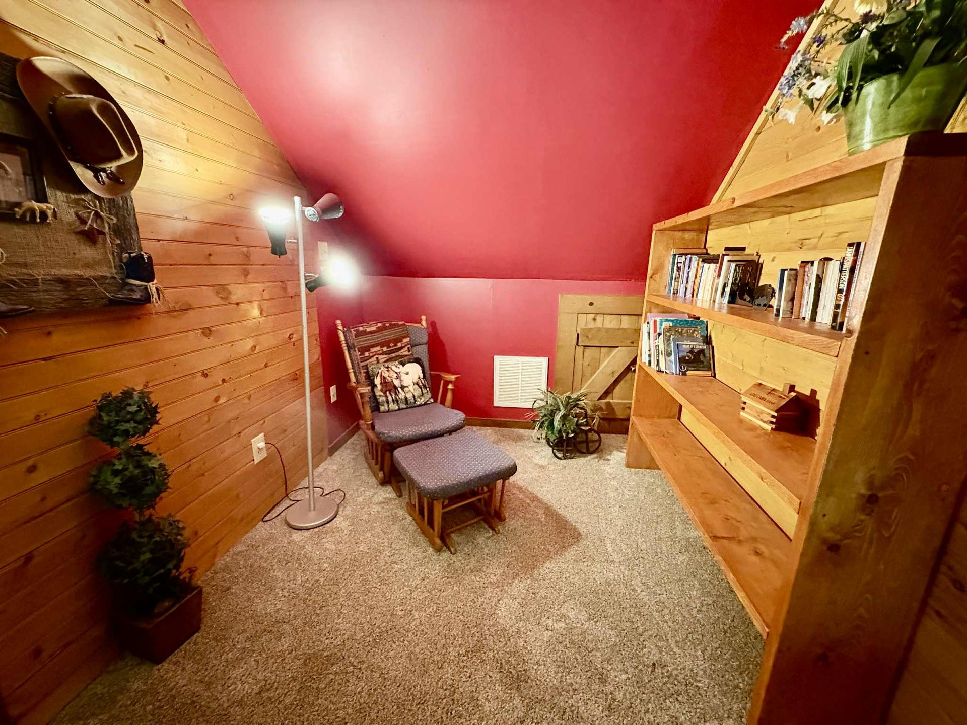 Cozy reading nook with wooden walls, red ceiling, rocking chair, bookshelf, and potted plants.