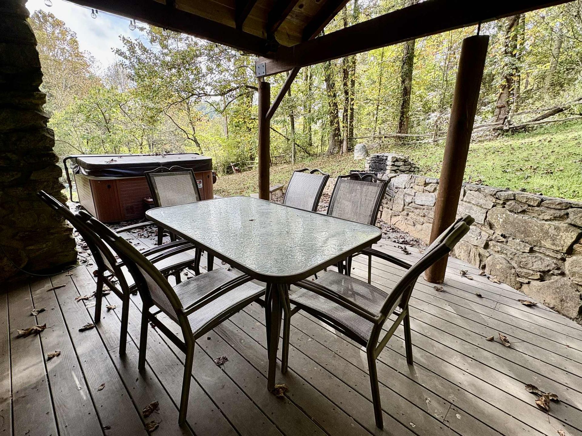 Patio with a table and chairs, hot tub, and forest background.