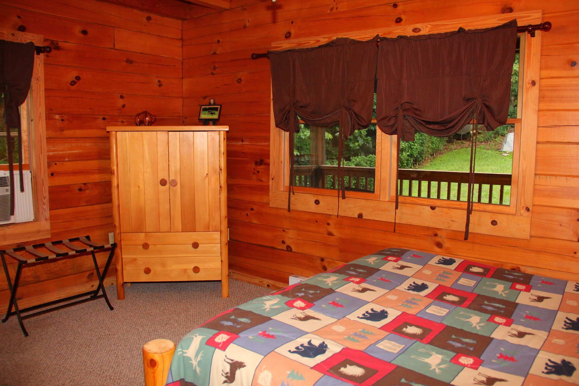 Rustic bedroom with wooden walls, bed, wardrobe, and windows overlooking a deck.