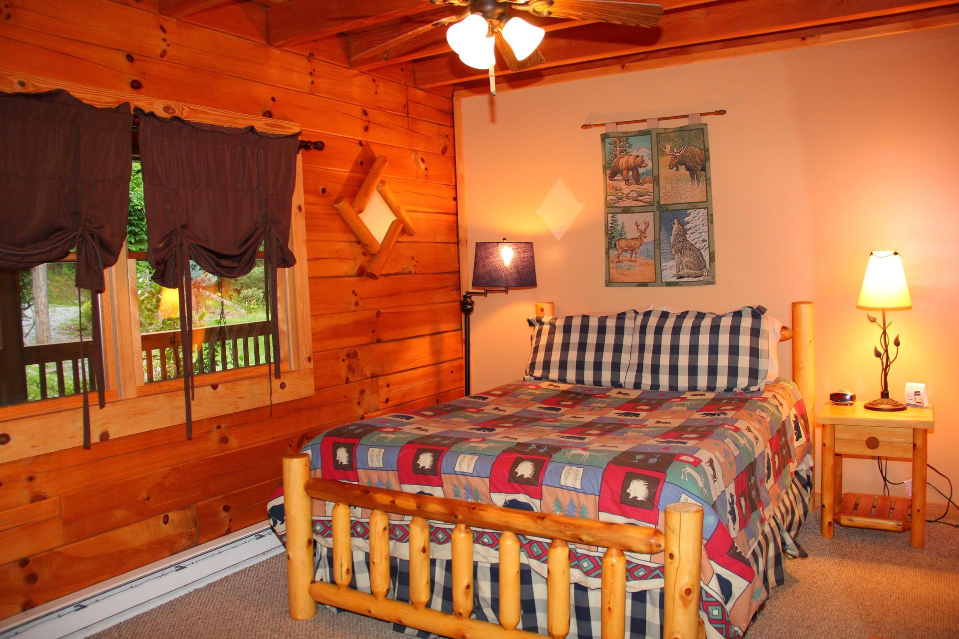 Cozy bedroom with log bed, quilt, and dark curtains. Log walls, beige walls, and a small nightstand with a lamp.