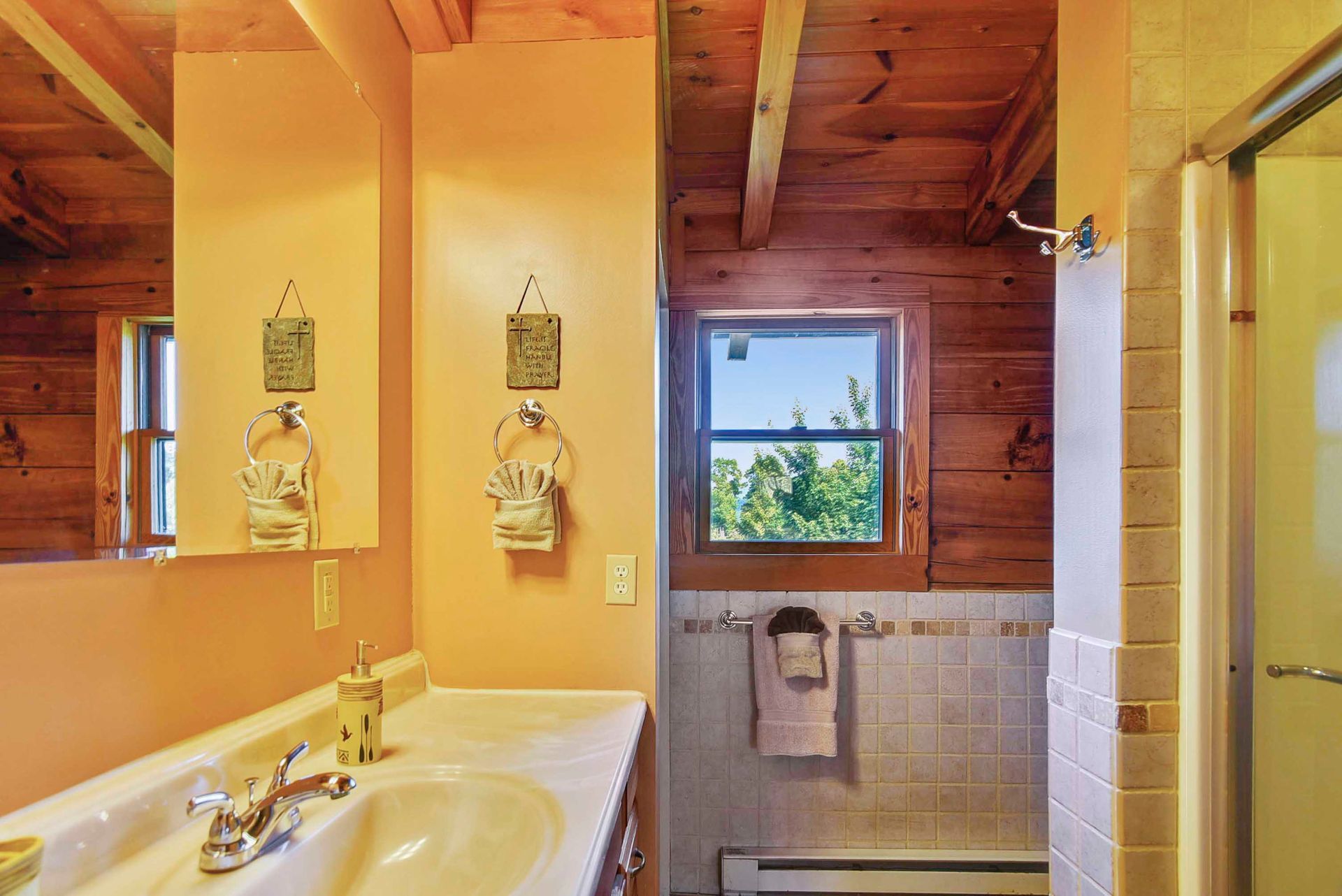 Bathroom with orange walls, wood paneling, white sink, and small window.
