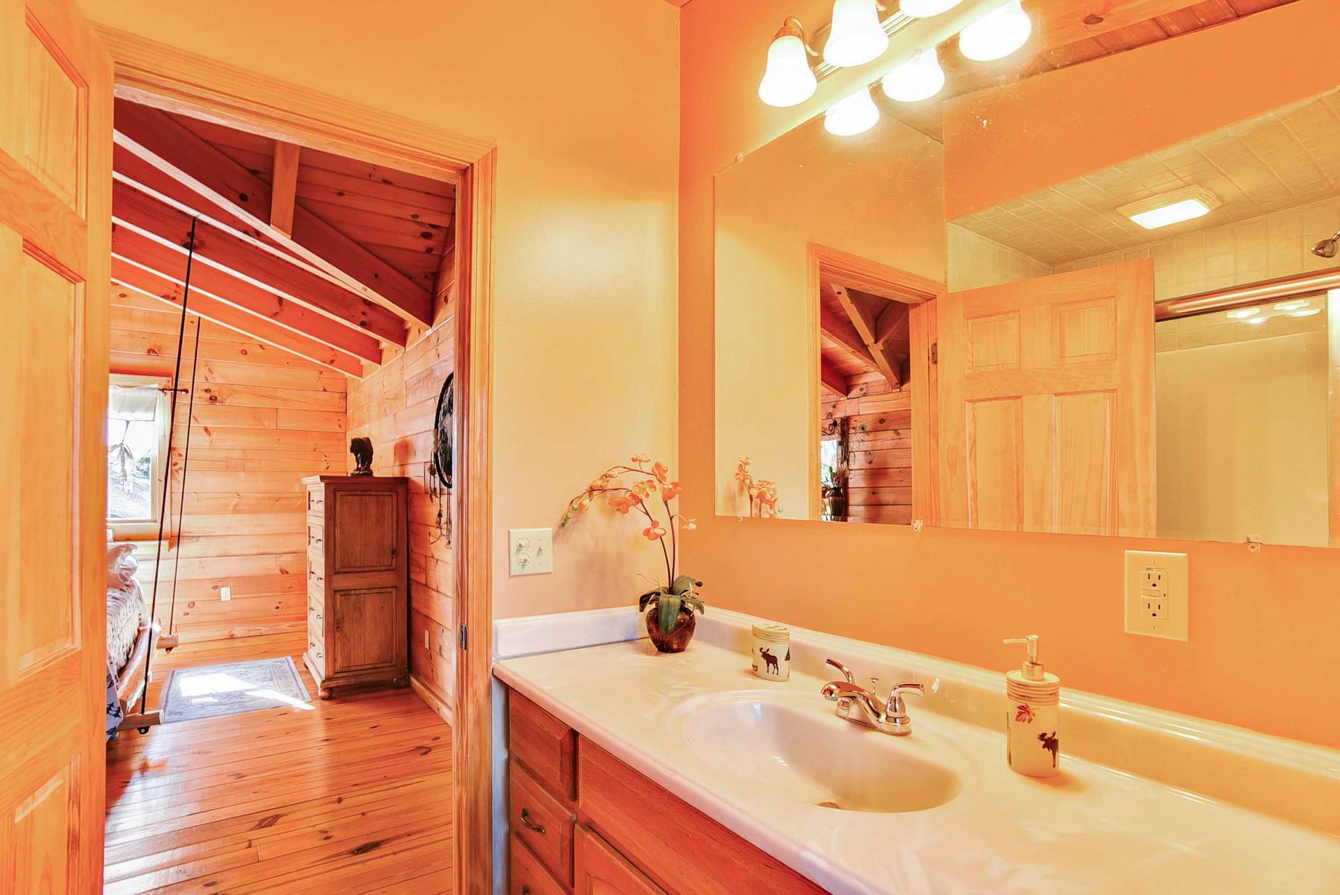Bathroom with a vanity and open doorway to a bedroom with wooden beams and walls.