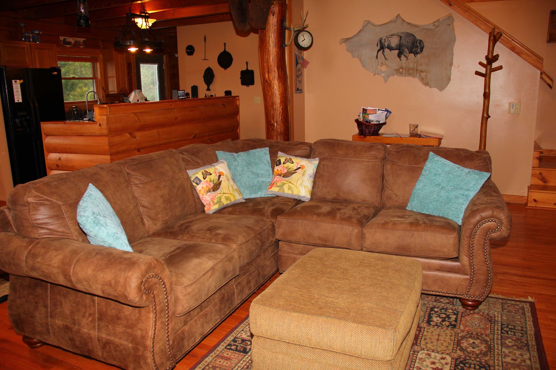 Living room with a brown leather sectional, ottoman, and buffalo mural.