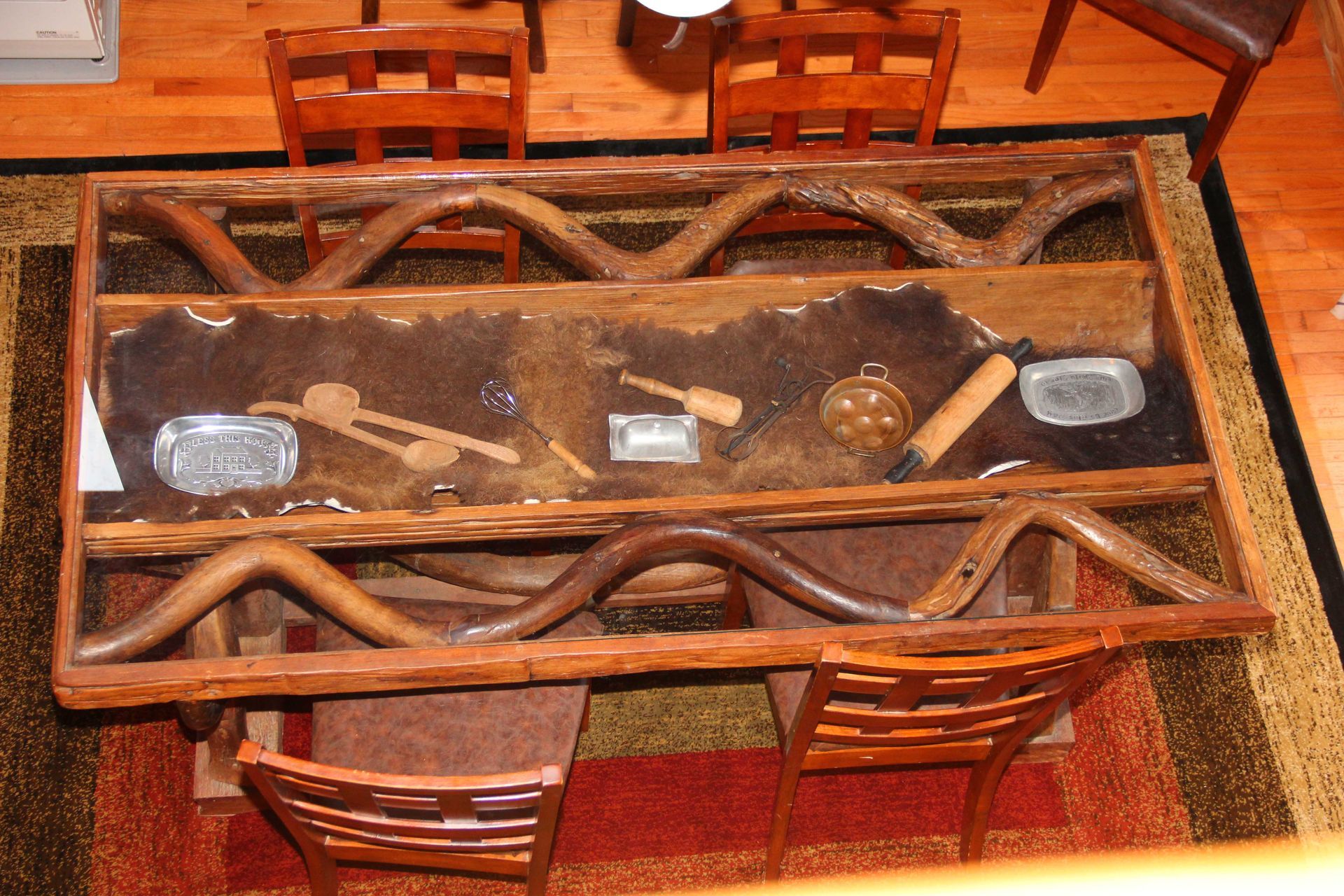 Rustic wood table with objects encased in resin, surrounded by wood chairs on a patterned rug.