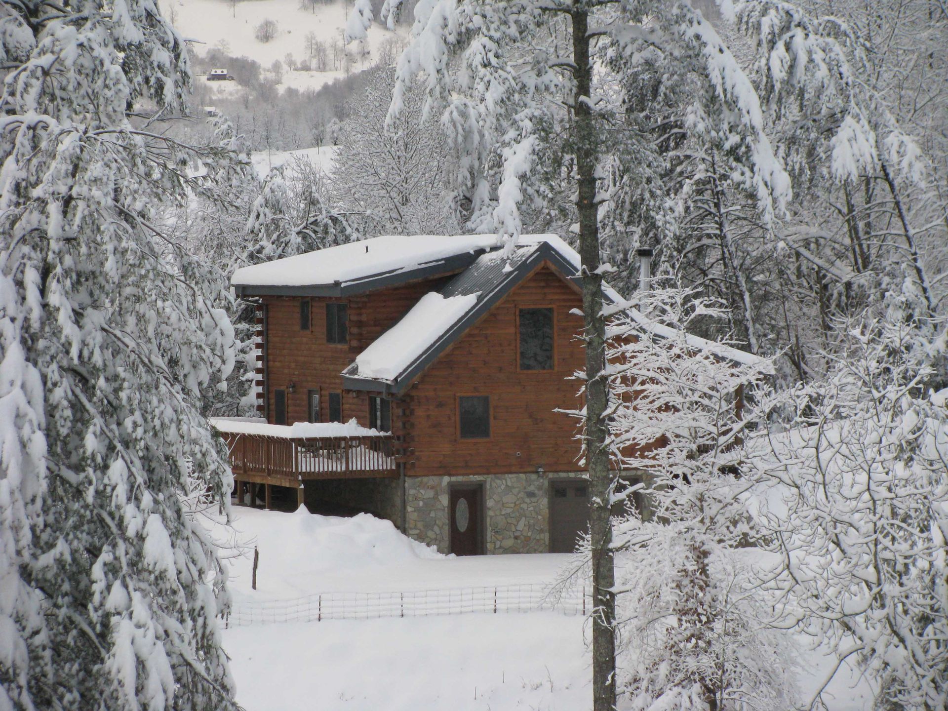 Snow-covered cabin in a forest, brown wood and stone, gray roof, snow on trees, winter scene.