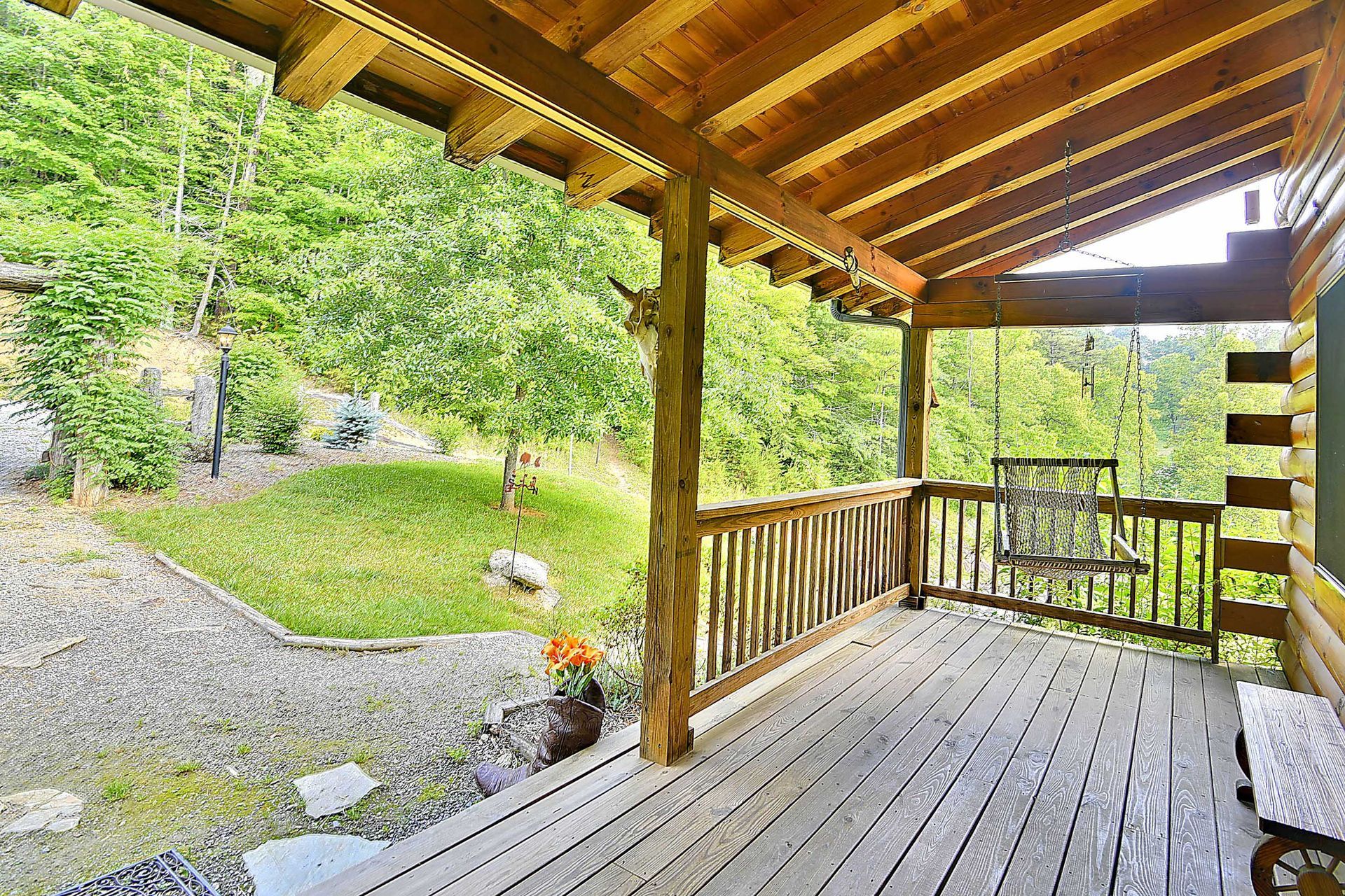 Wooden porch overlooking a grassy yard and trees. A swing hangs on the right.