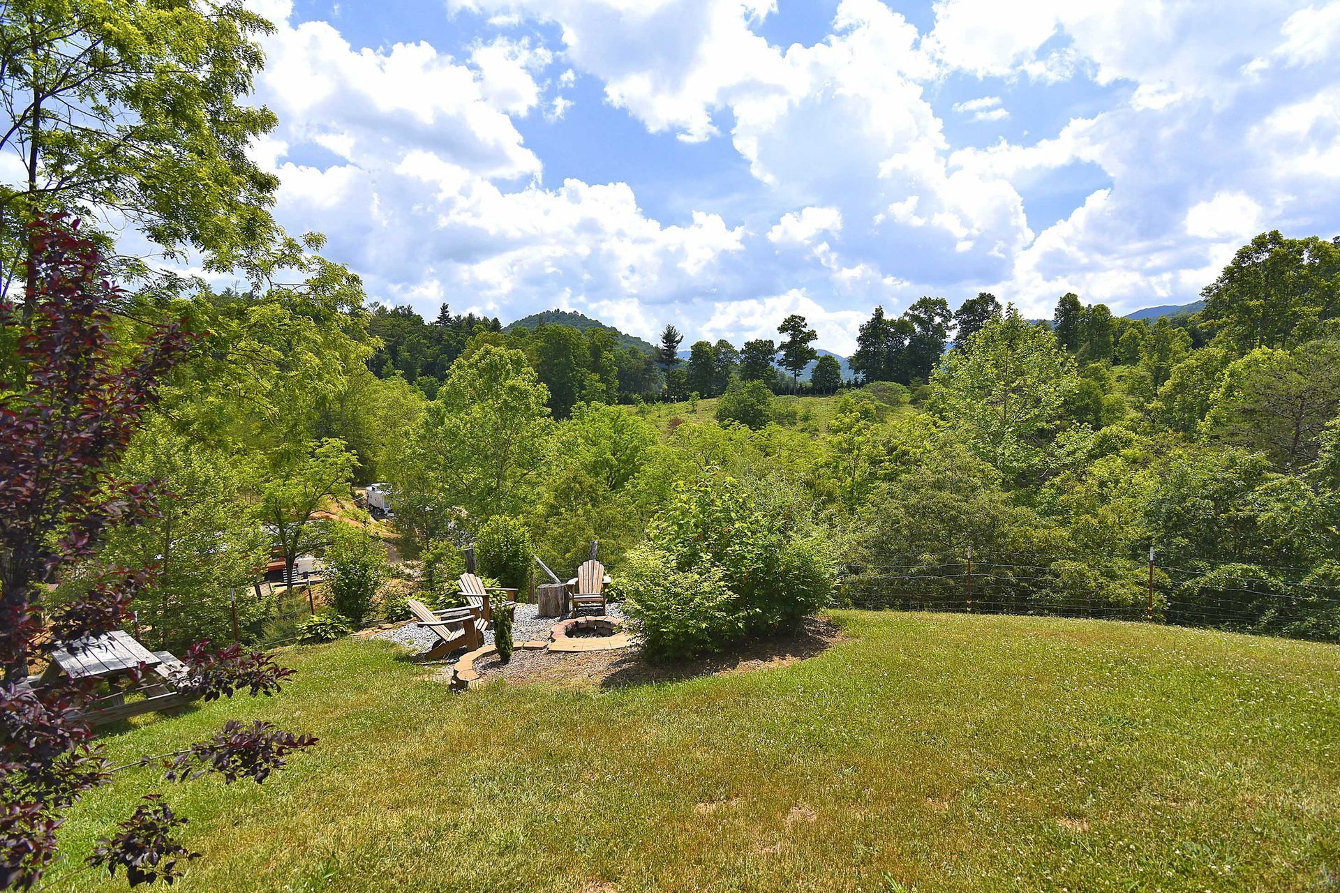 Green landscape with grassy lawn, trees, and cloudy blue sky.
