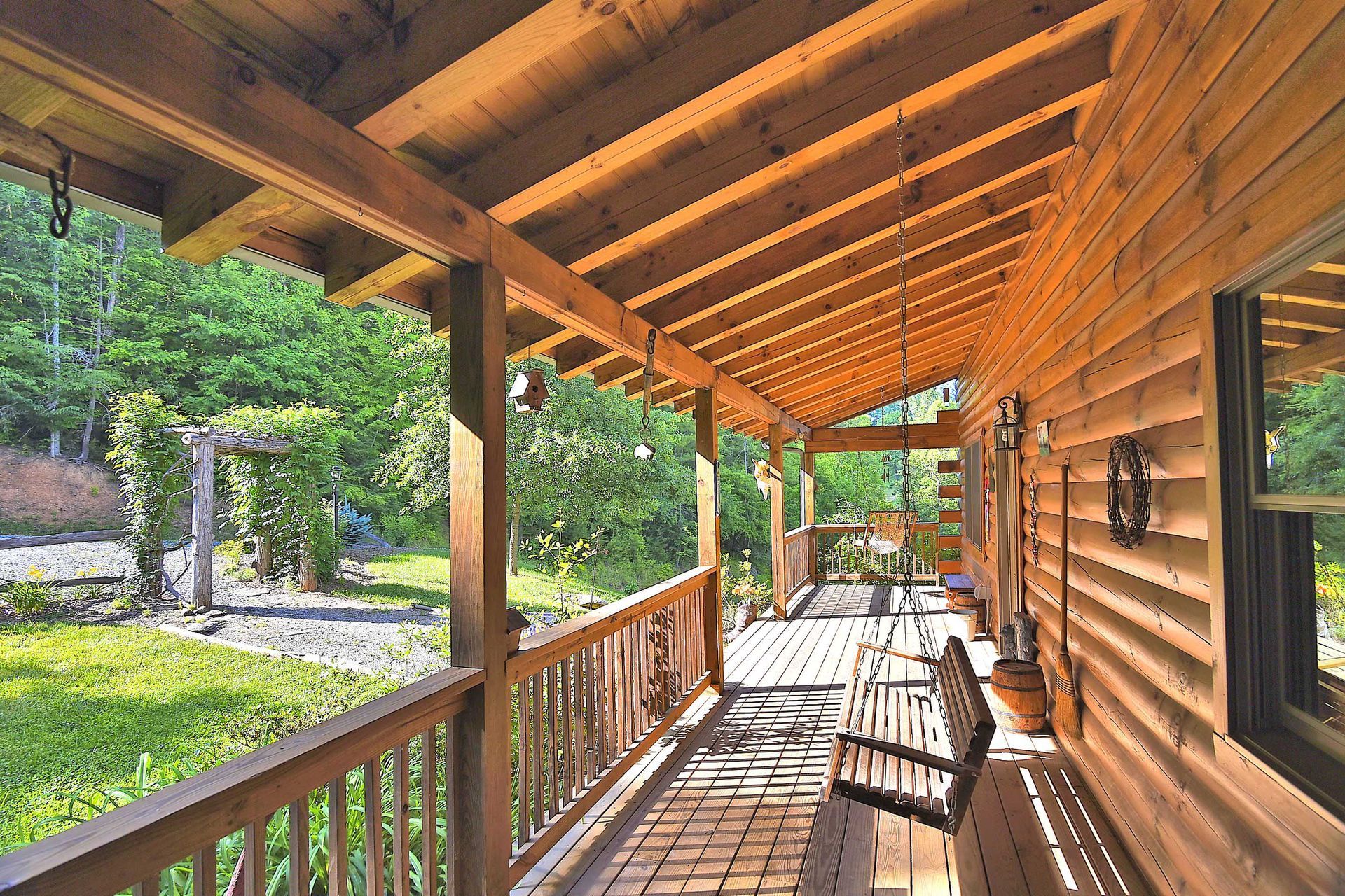 Wooden cabin porch with a swing and railing overlooking a green yard and trees.
