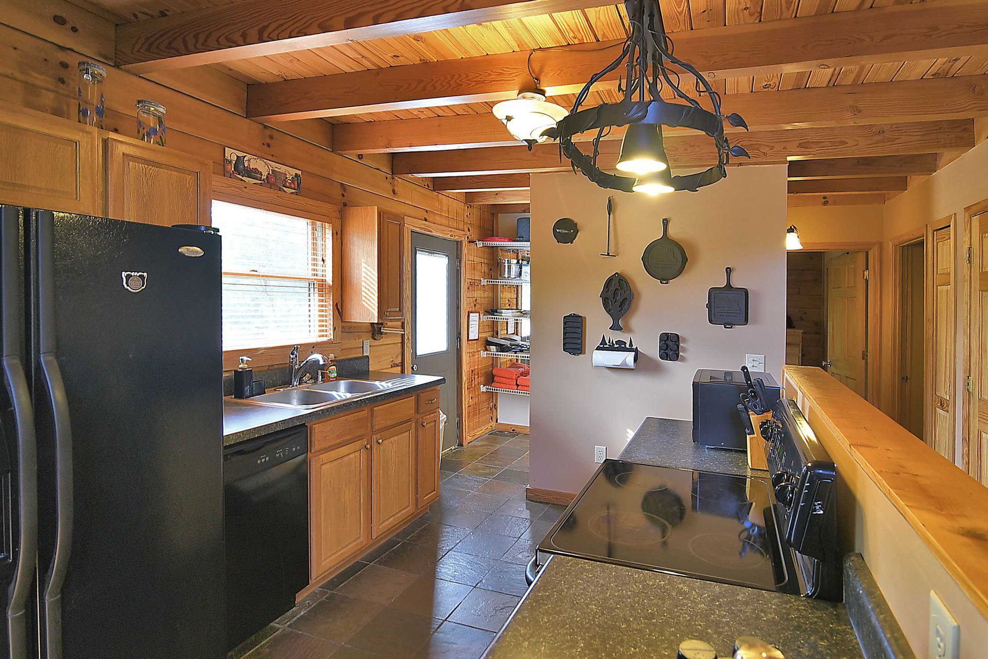 Kitchen with wooden beams, black appliances, and neutral-colored cabinets. Pots hang on the wall.